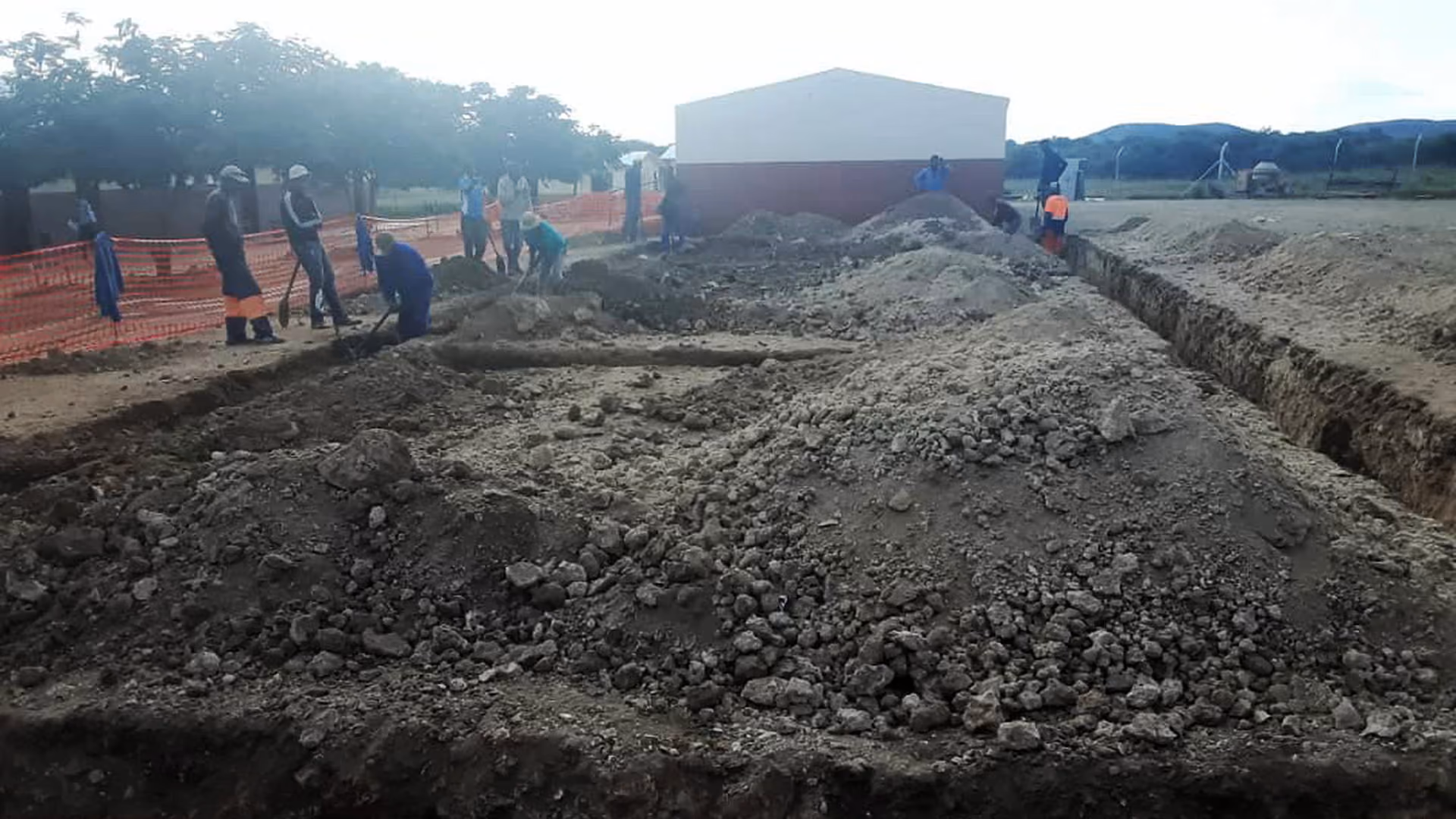 Bauarbeiter graben und bewegen Erde vor einem Gebäude auf einer Baustelle im Freien.