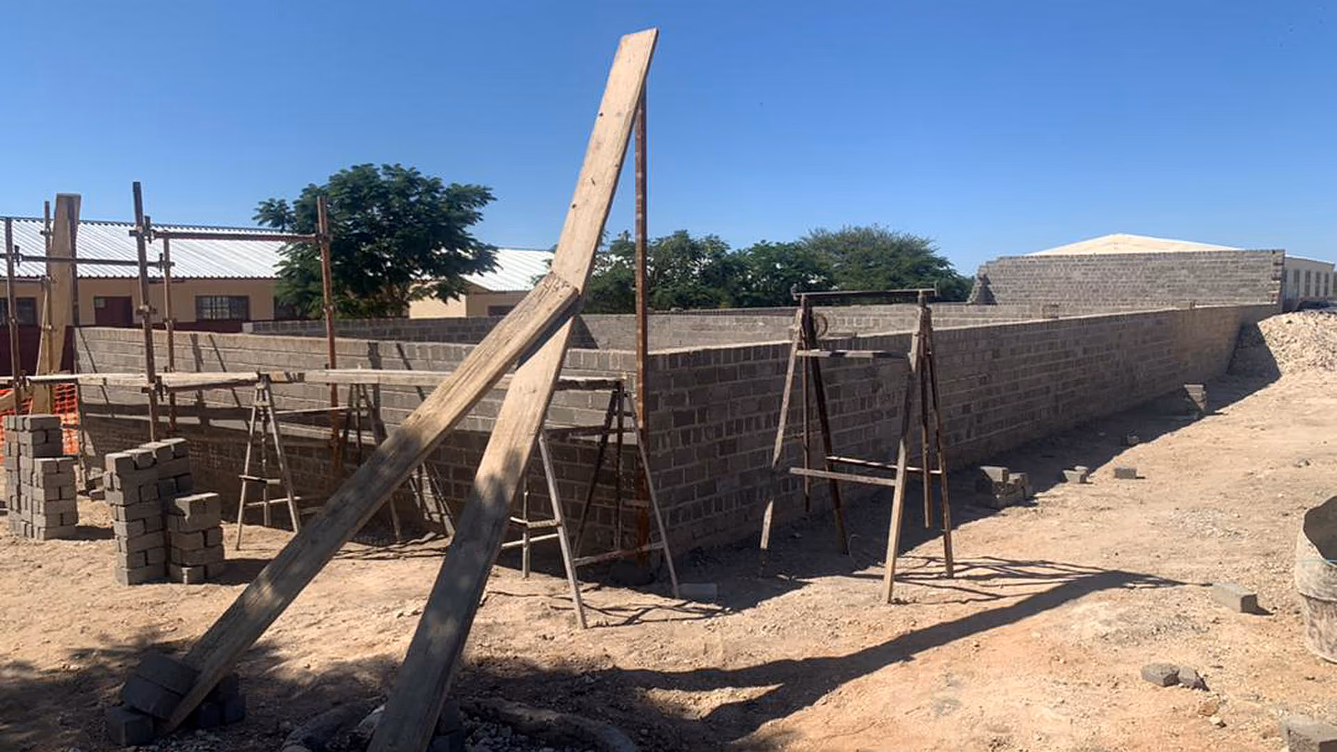 Baustelle mit halbfertiger Mauer aus Ziegelsteinen, Gerüst und Baugeräten im Freien.