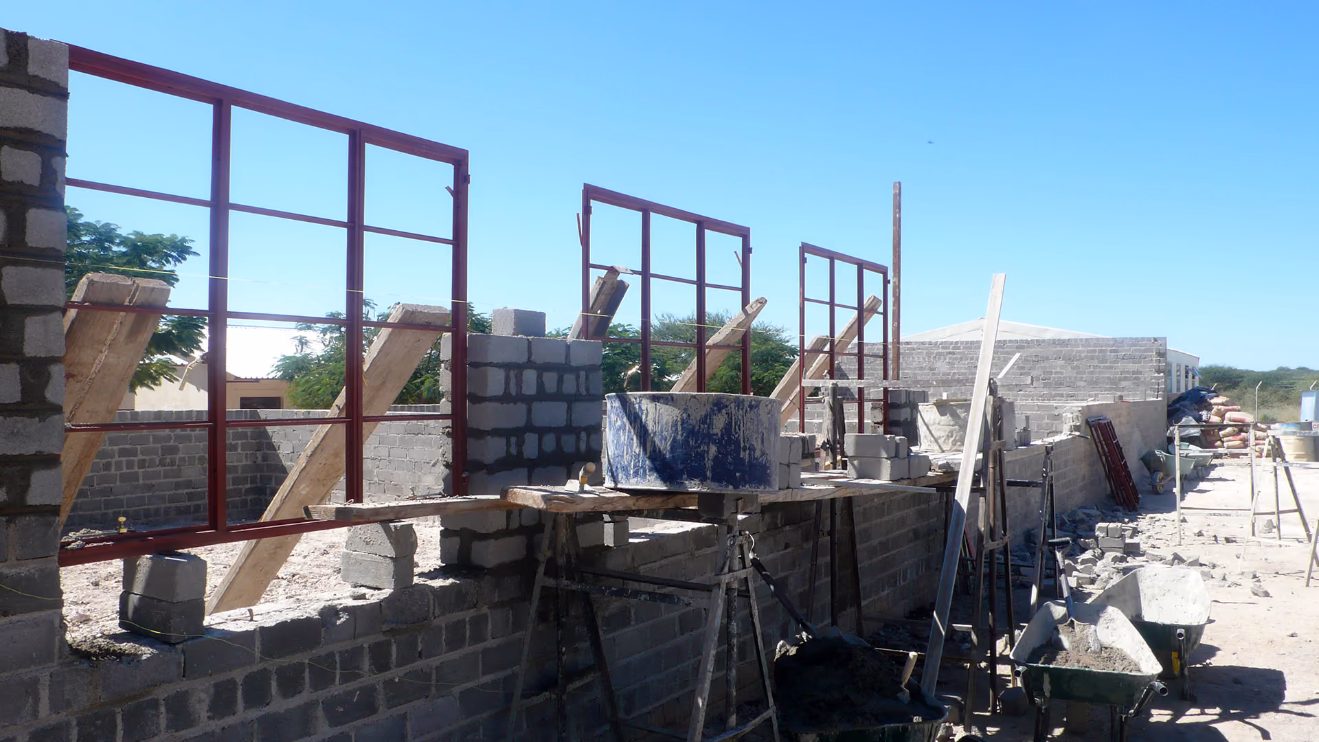 Baustelle eines Gebäudes mit Backsteinmauern, Metallfensterrahmen und Baumaterial unter blauem Himmel.