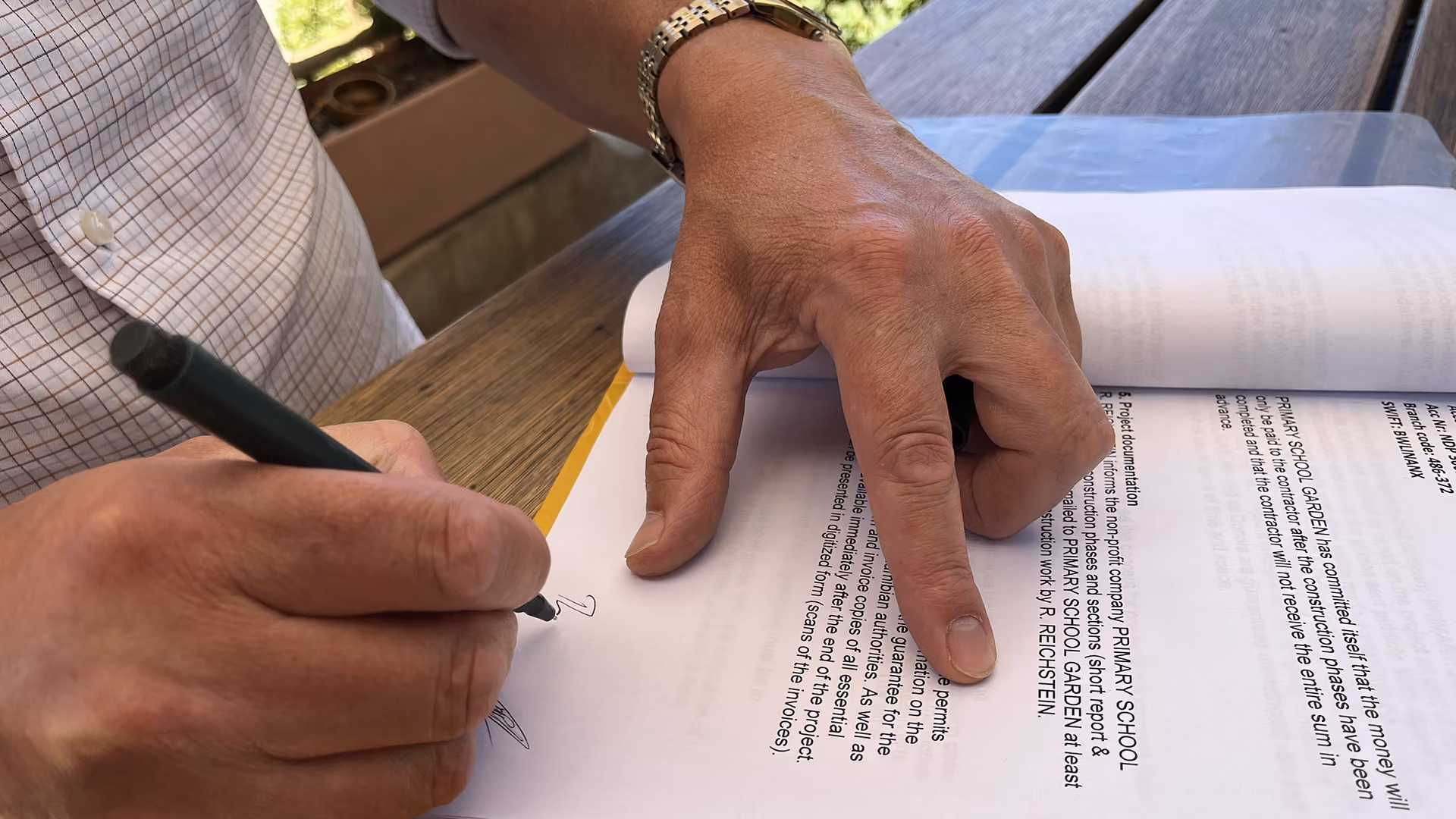 Person unterschreibt mit einem Stift ein Dokument auf einem Holztisch.