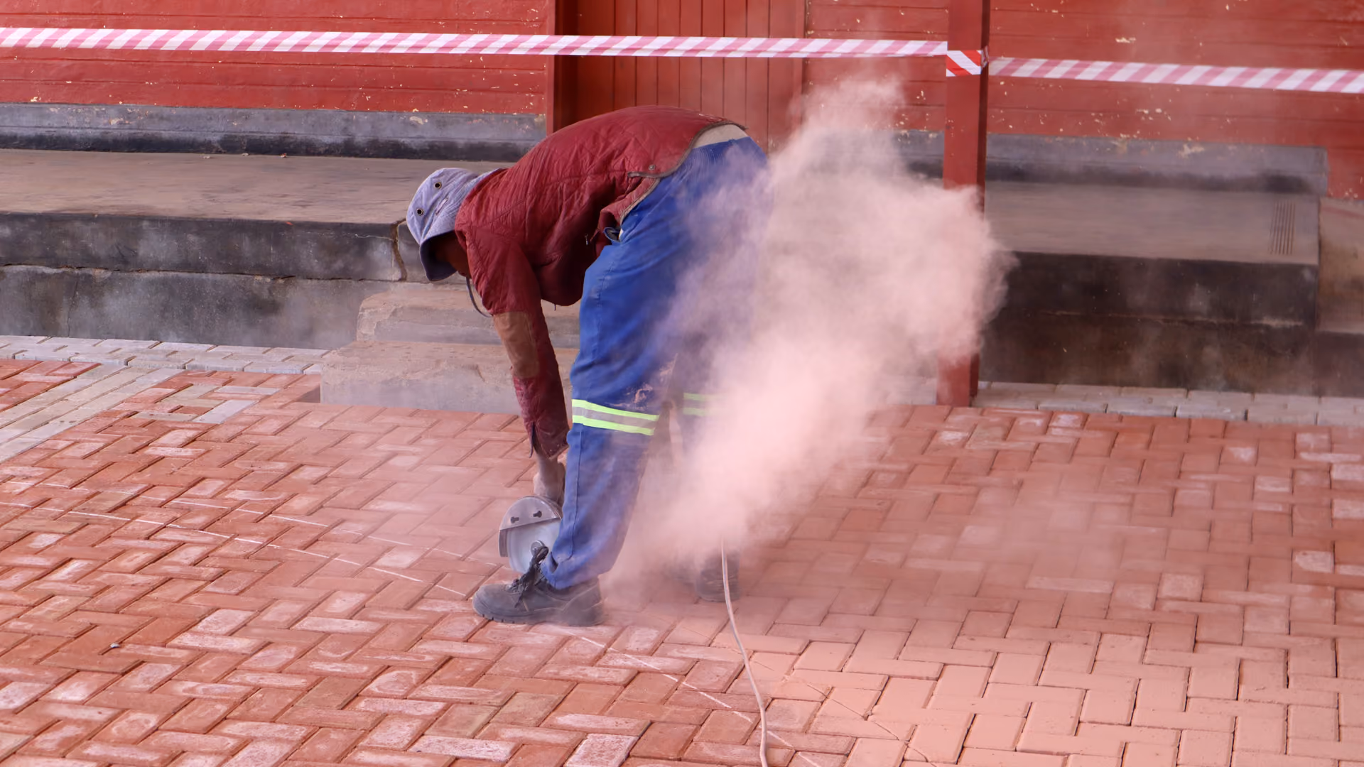 Ein Bauarbeiter schneidet ziegelrote Pflastersteine, dabei entsteht Staubwolke.