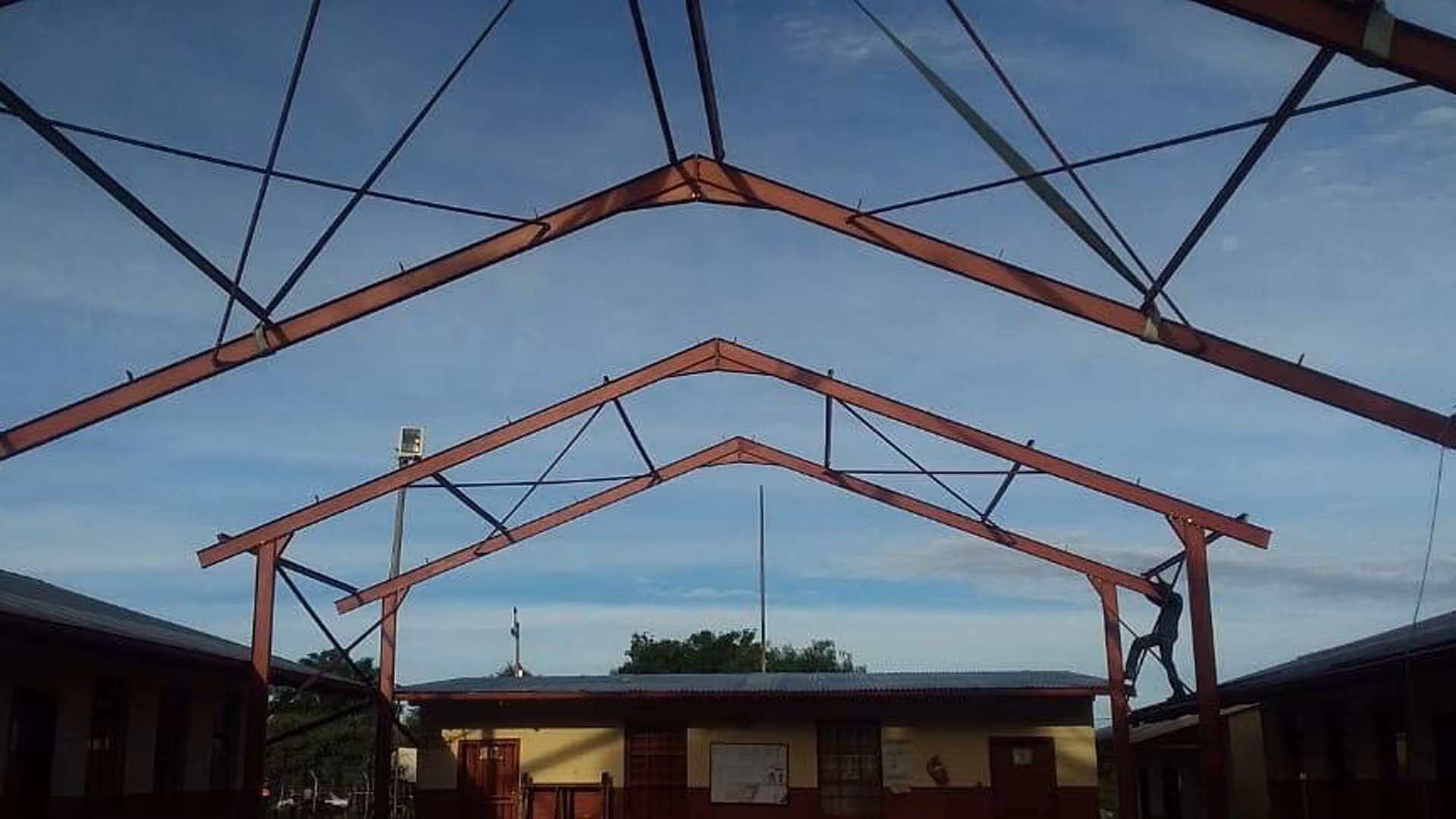Ein Mann klettert auf ein rotes Stahlgerüst in einem Schulhof mit blassem Himmel im Hintergrund.