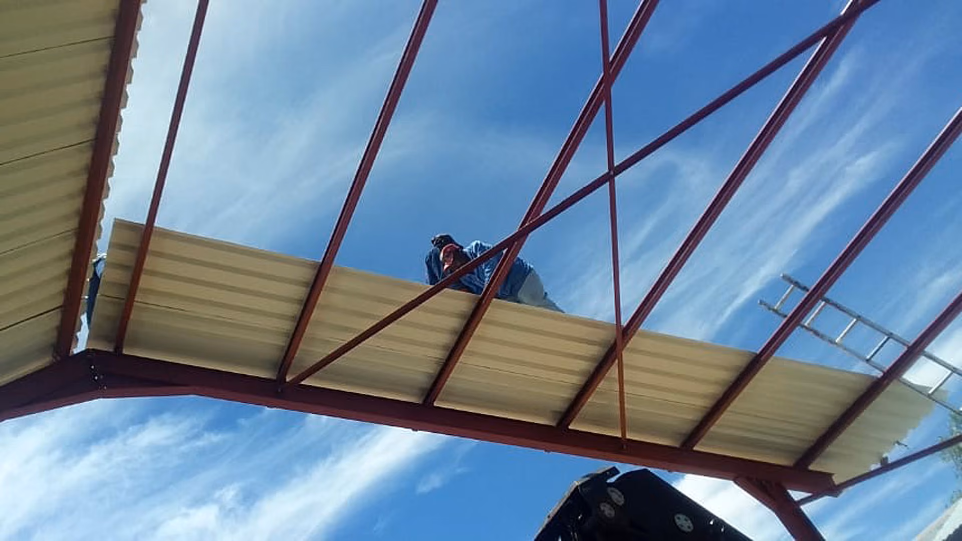 Person auf einer Metallkonstruktion montiert Dachplatten vor blauem Himmel.