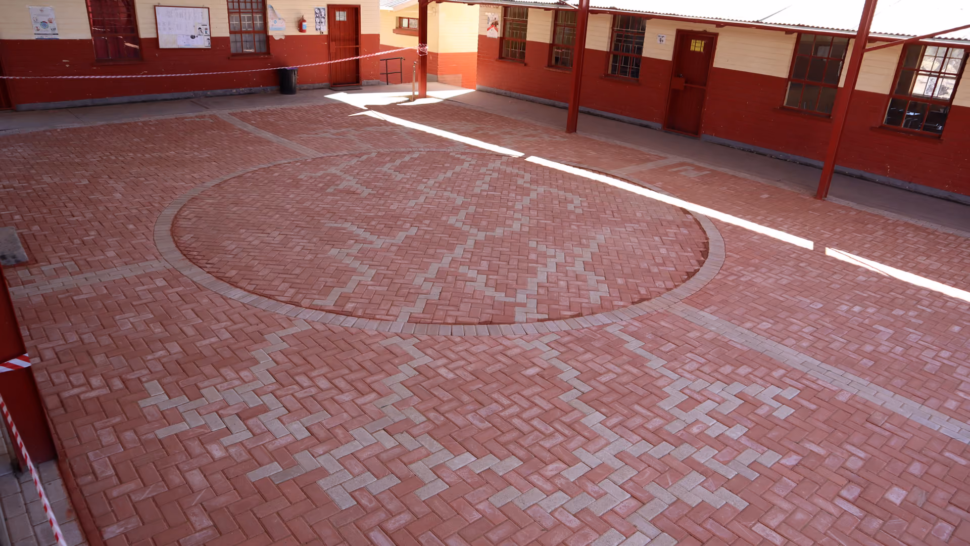 Hinterhof mit rotbraunen Ziegeln und geometrischen Mustern in einer Schulumgebung.