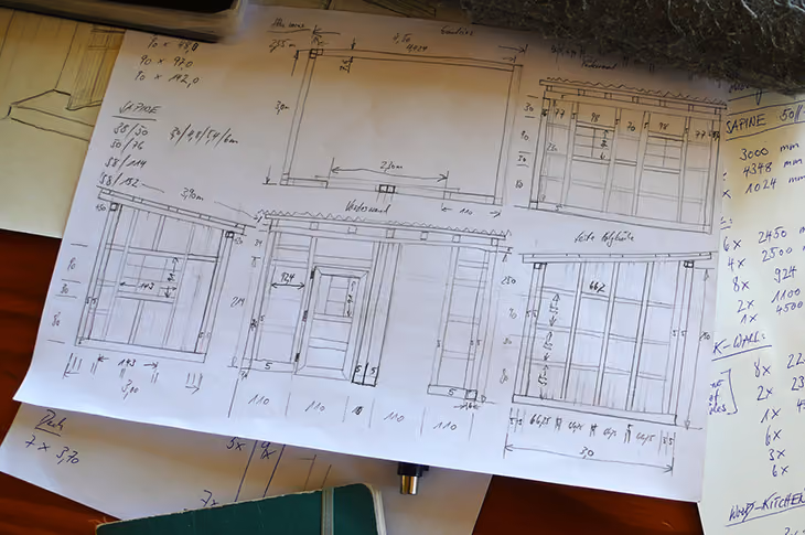 Handgezeichnete Baupläne für ein Gartenhaus mit Maßen und Notizen auf Papier.