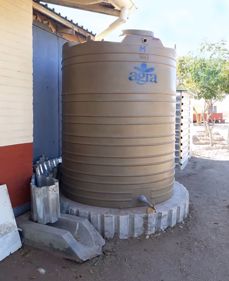 Großer brauner Wassertank neben einem Gebäude mit Abflussrohr und Betonbasis.