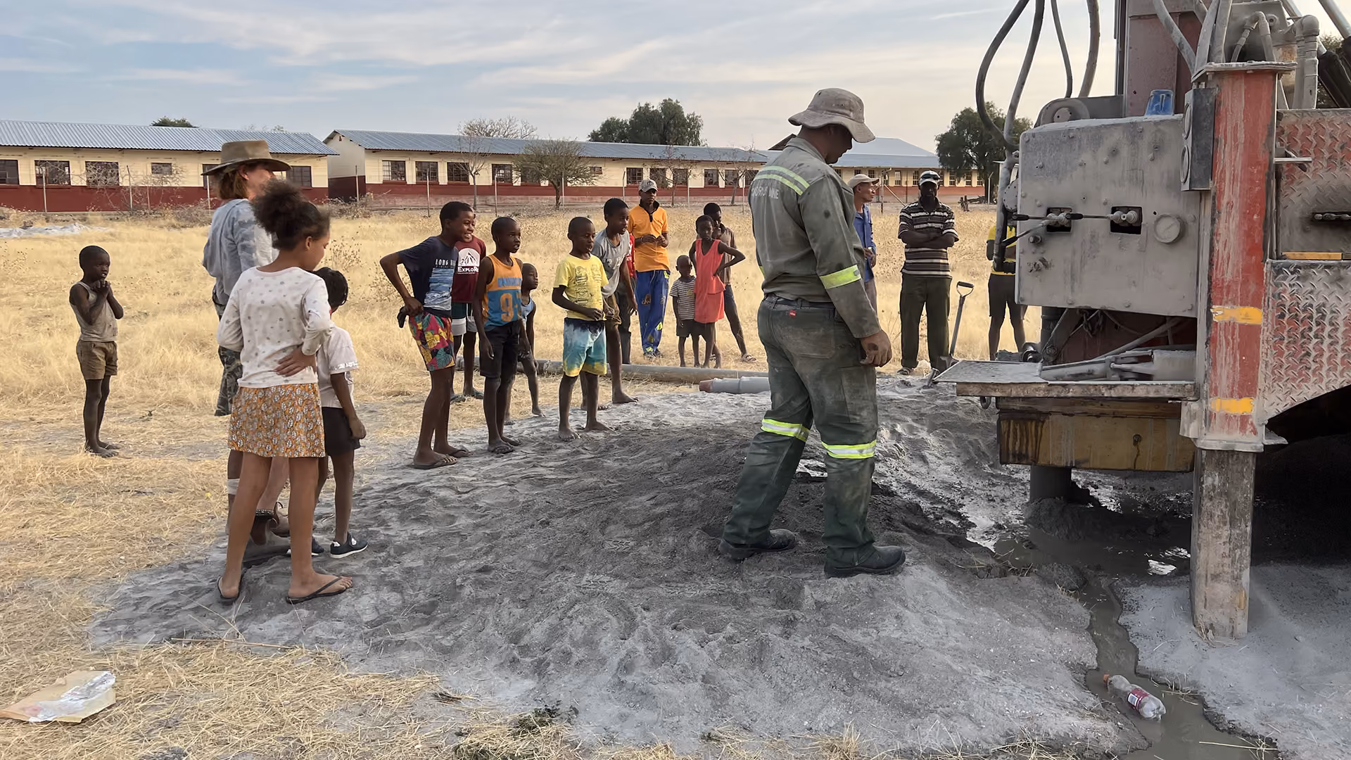 Gruppe von Kindern und Erwachsenen beobachtet eine Bohrmaschine bei der Arbeit auf einem trockenen Feld.