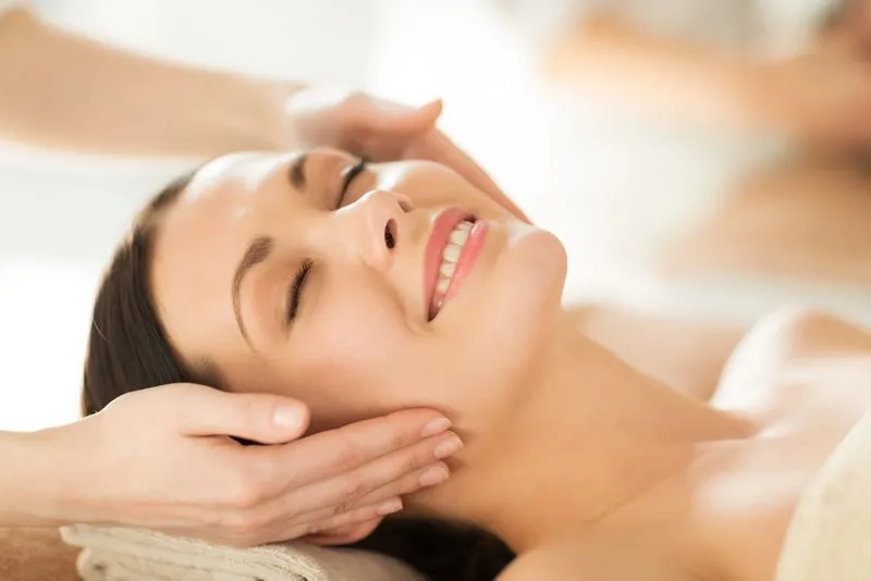 Woman with closed eyes smiling while receiving a facial massage.