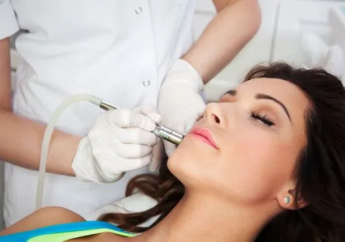 Woman receiving a facial treatment with a handheld device by a skincare professional wearing gloves.