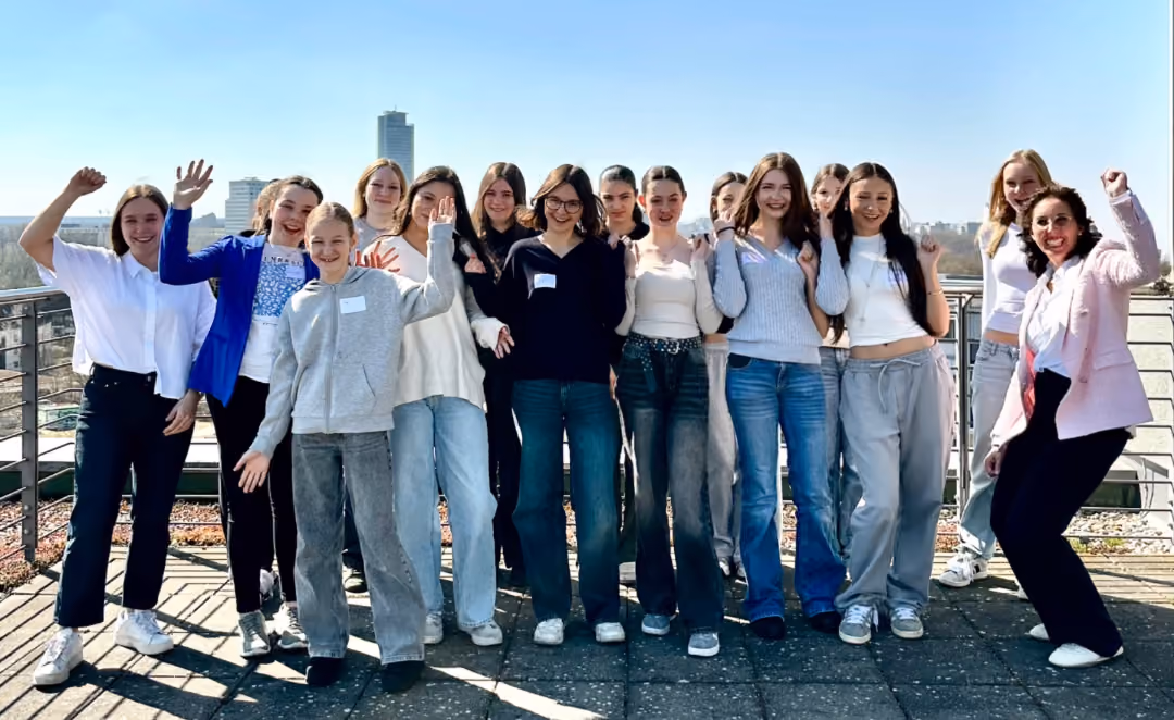 Gruppe junger Mädchen jubelt auf einer Dachterrasse vor Stadtsilhouette und blauem Himmel
