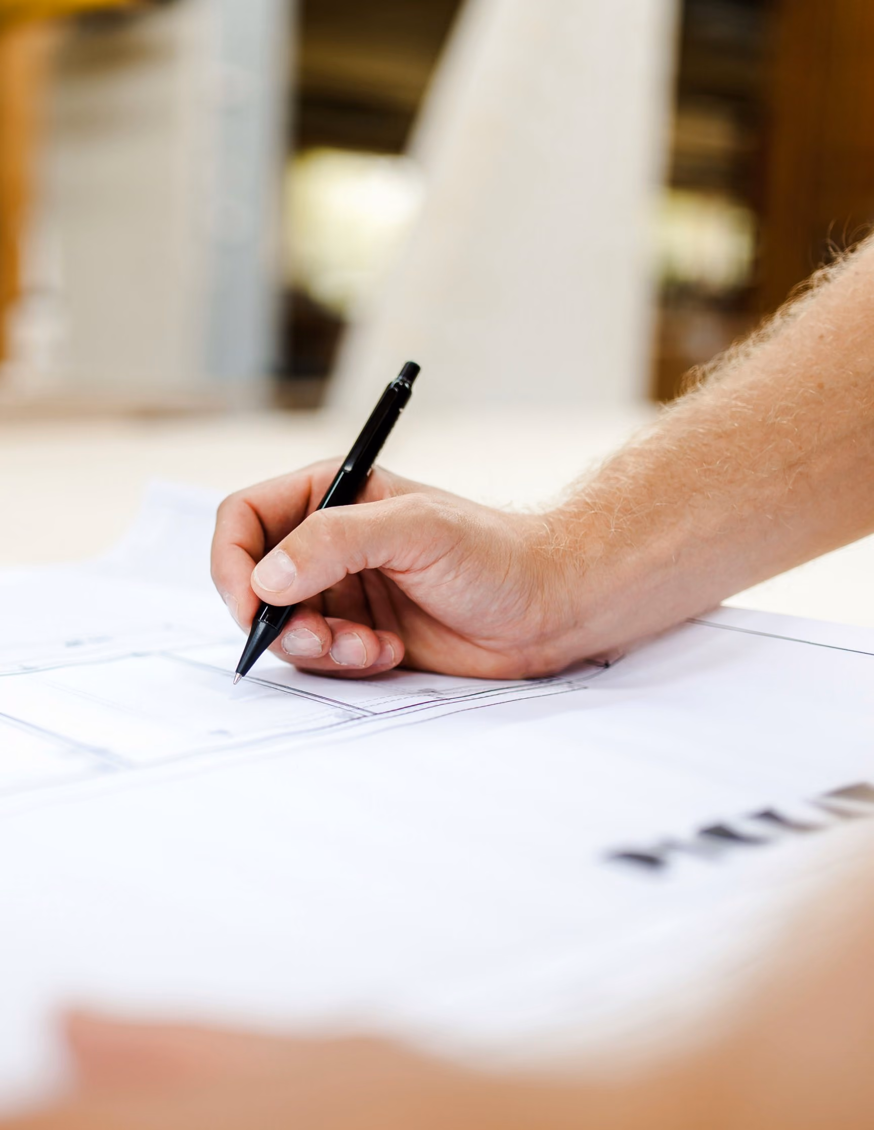 Hand zeichnet mit einem Stift Linien in einen Plan auf einem hellen Tisch