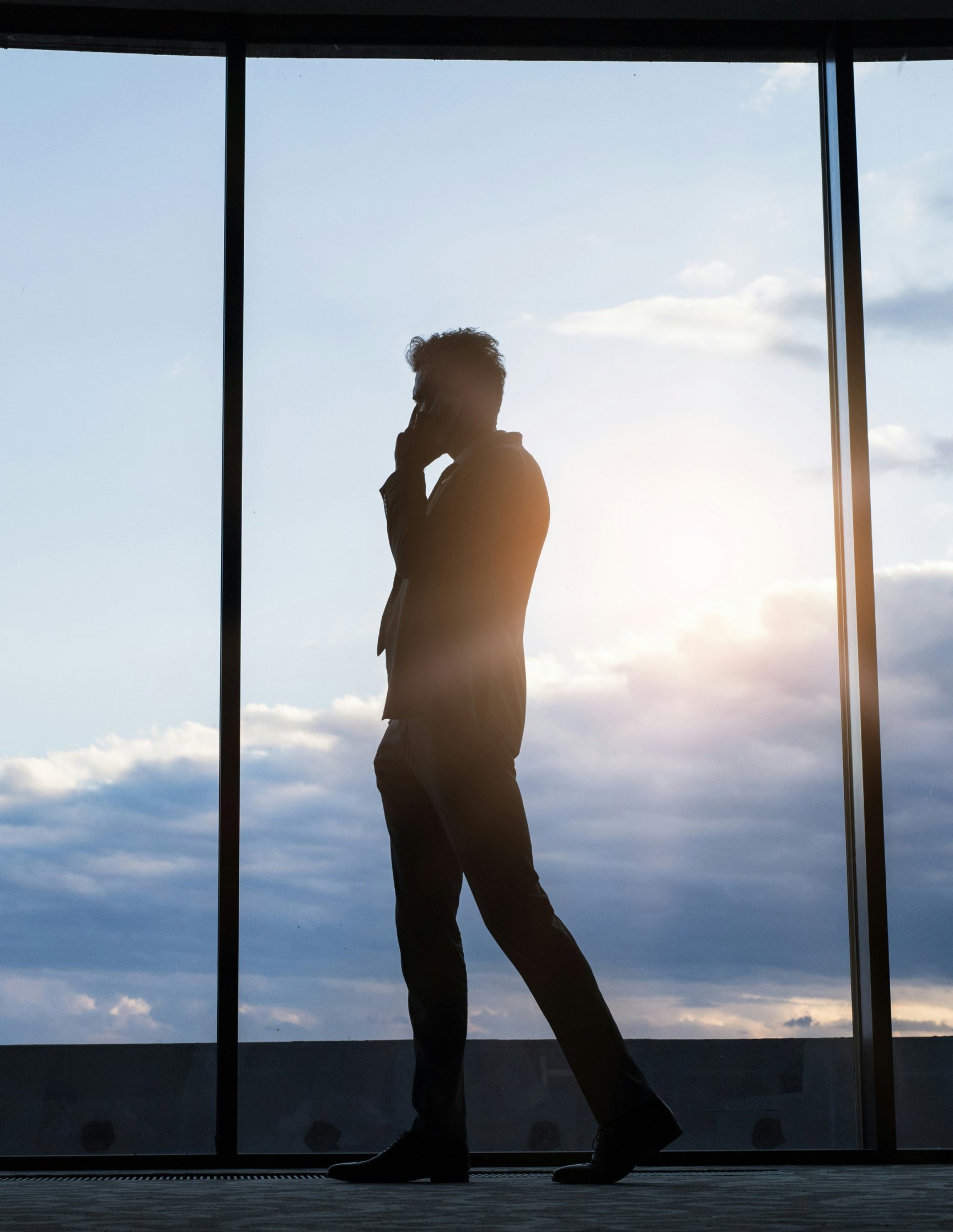 Silhouette eines telefonierenden Mannes vor einer bodentiefen Fensterfront im Gegenlicht