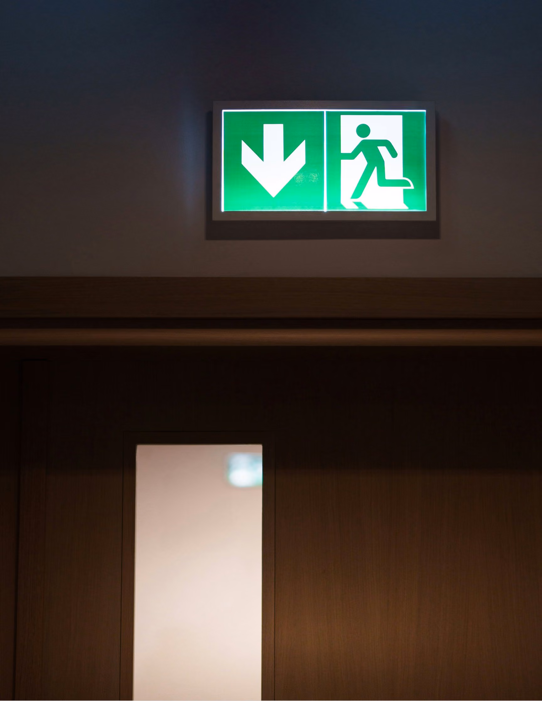 Beleuchtetes grünes Notausgangsschild über einer Tür in einem dunklen Flur