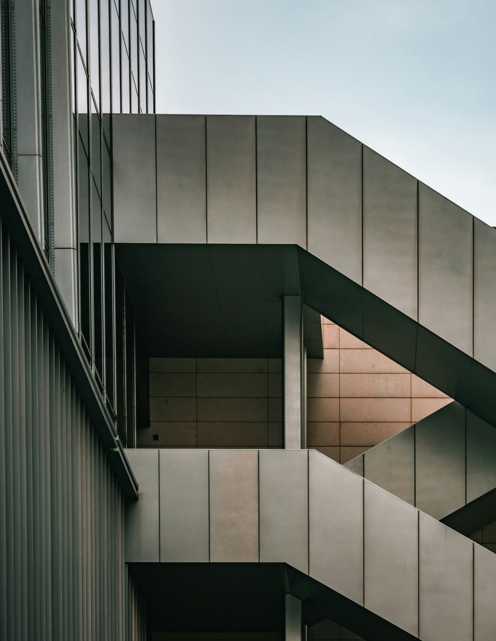 Betonfassade eines Gebäudes mit diagonal verlaufenden Treppenläufen vor hellem Himmel