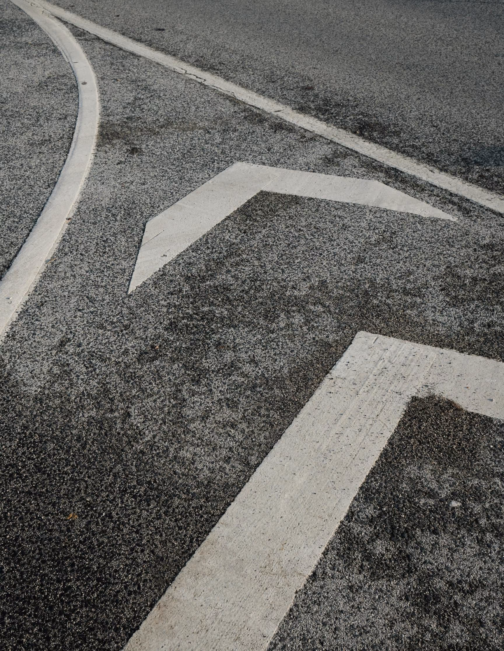 Weiße Richtungspfeile als Fahrbahnmarkierung auf grauem Asphalt
