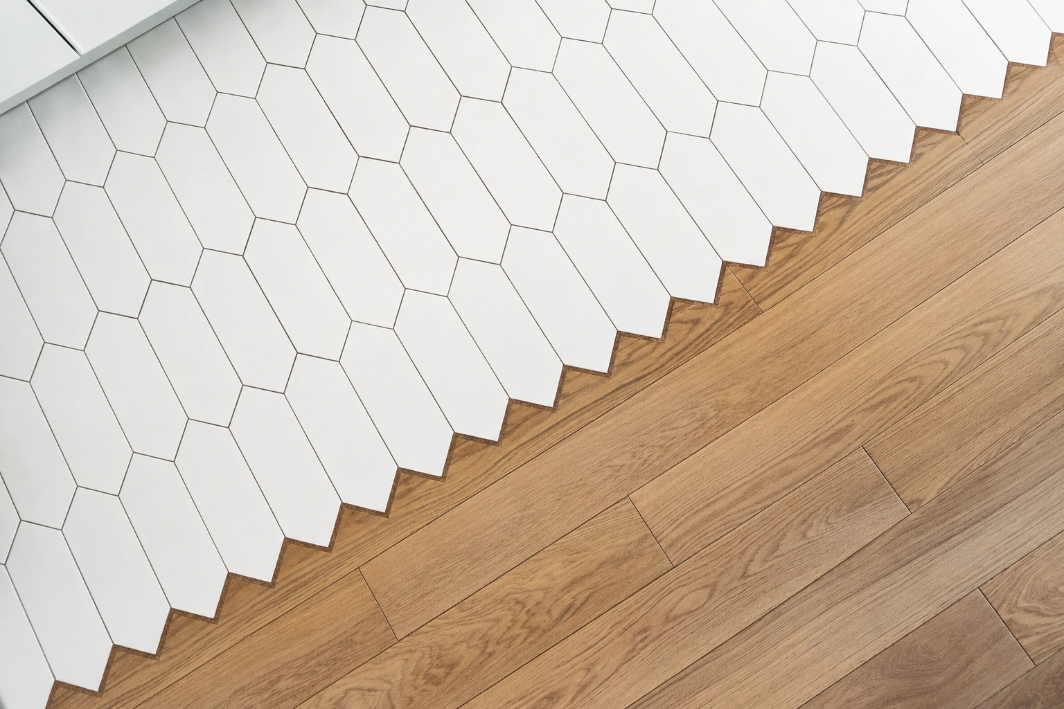 Metal edging trim between white hexagon tile and wood flooring