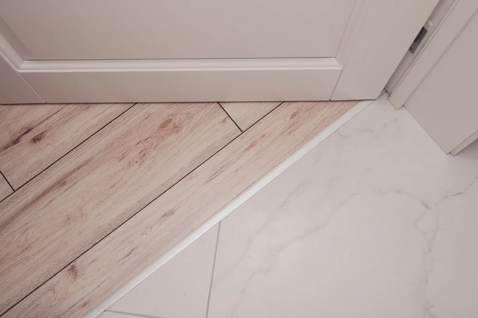 Close view of edging between pale wood planks and marble tile
