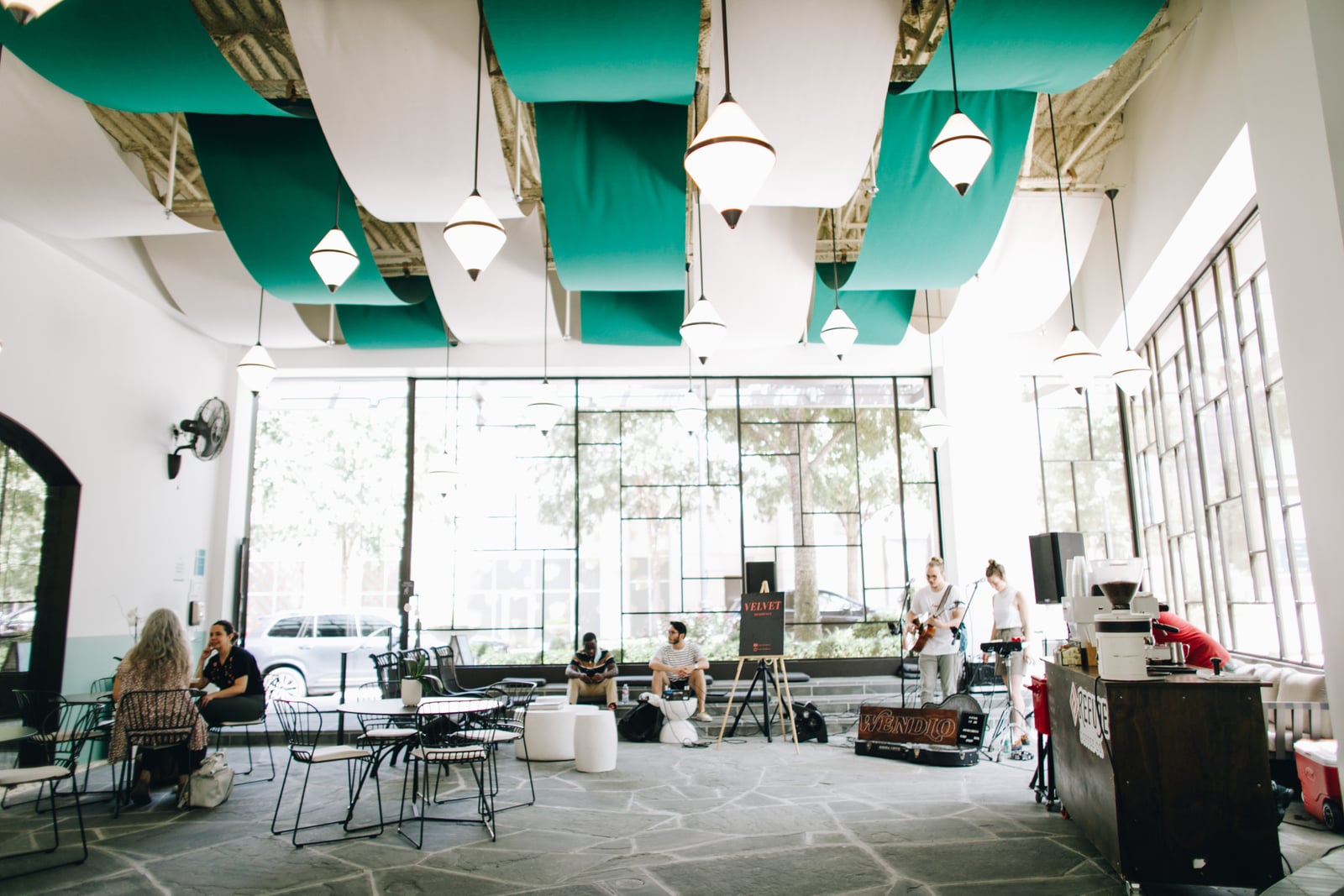 Intérieur lumineux d’un café, avec des panneaux de plafond verts et blancs, des sièges et des musiciens