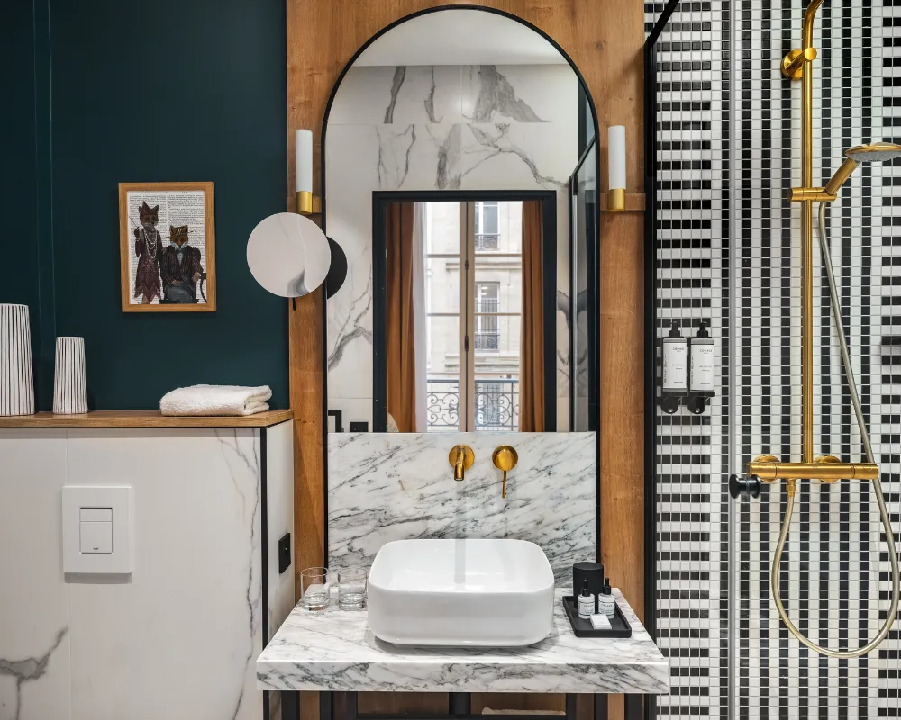 Salle de bain en marbre et bois avec vasque à robinetterie dorée, miroir arqué et douche à mosaïque noire et blanche