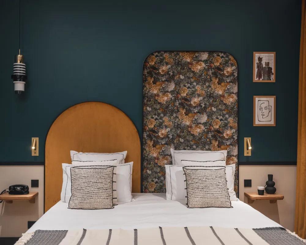 Deux lits jumeaux avec arche dorée et panneau à motif minéral, appliques murales et tableaux encadrés sur mur bleu paon