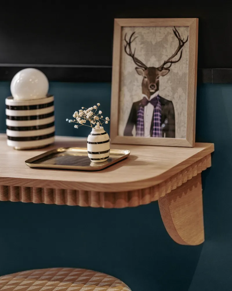 Tablette murale en bois avec lampe boule, vase floral et portrait illustré d'un cerf en costume, sur fond bleu paon