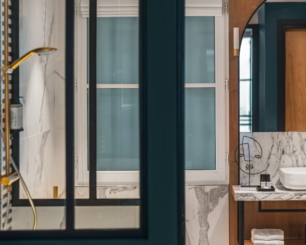Douche à robinetterie dorée en marbre veiné, fenêtre à petits carreaux noirs et vasque en arrière-plan