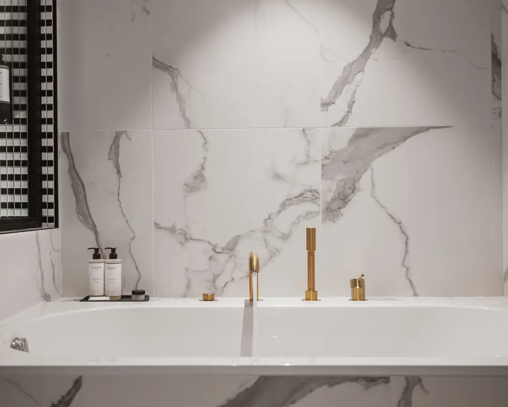 Baignoire blanche encastrée en marbre veiné avec robinetterie dorée, flacons de toilette posés au bord