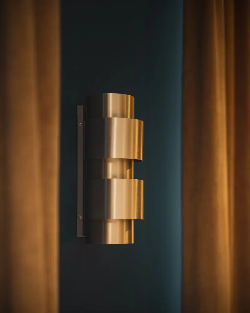 Applique dorée à anneaux superposés fixée sur mur bleu paon, encadrée de rideaux dorés tombants