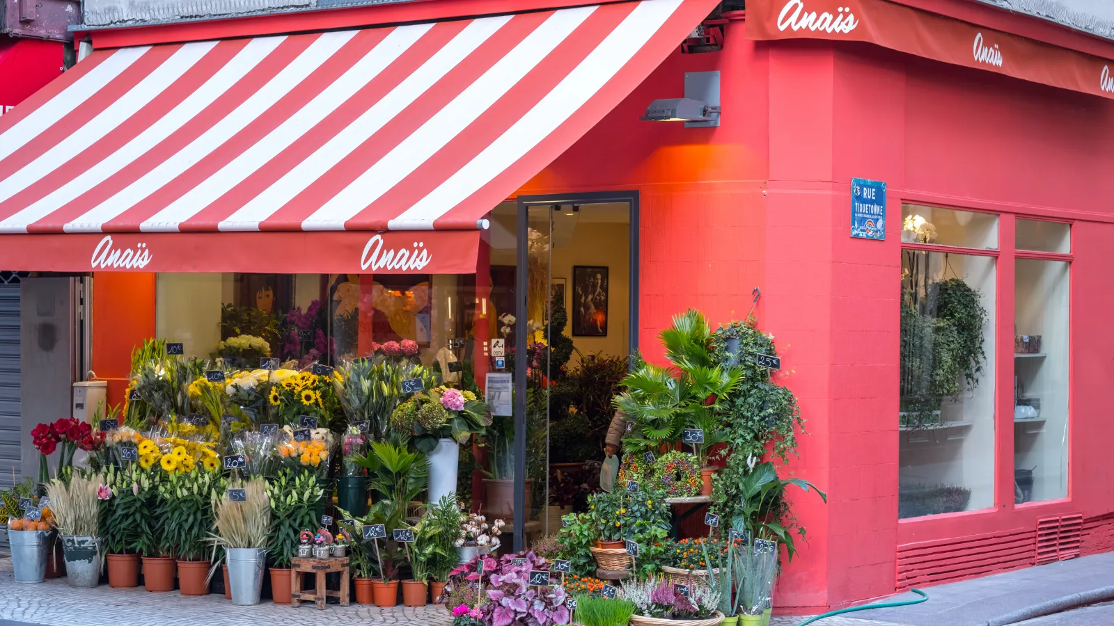 une boutique de fleurs à façade rouge et auvent rayé, bouquets exposés en devanture sur le trottoir