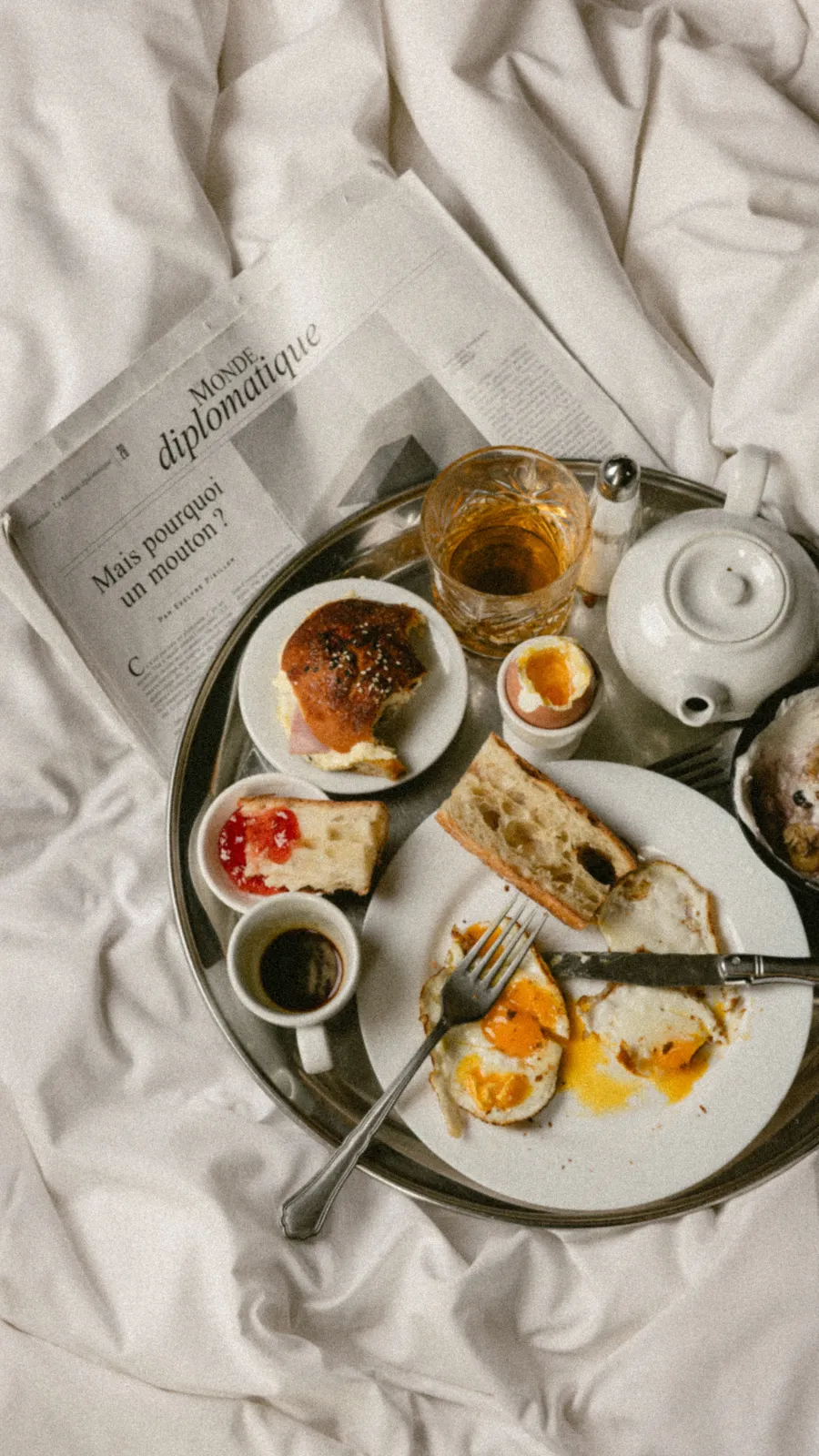 Miniature en gros plan du plateau de petit-déjeuner sur le lit, avec confitures, œufs au plat et carte de menu posée à côté