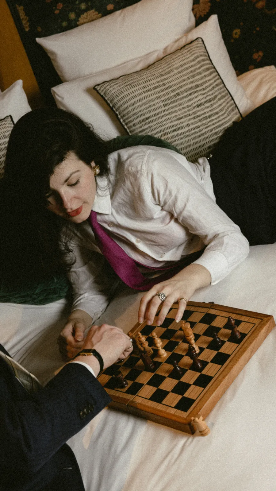 vue plongeante d'une femme jouant aux échecs allongée sur un lit, échiquier en bois posé entre elle et son partenaire