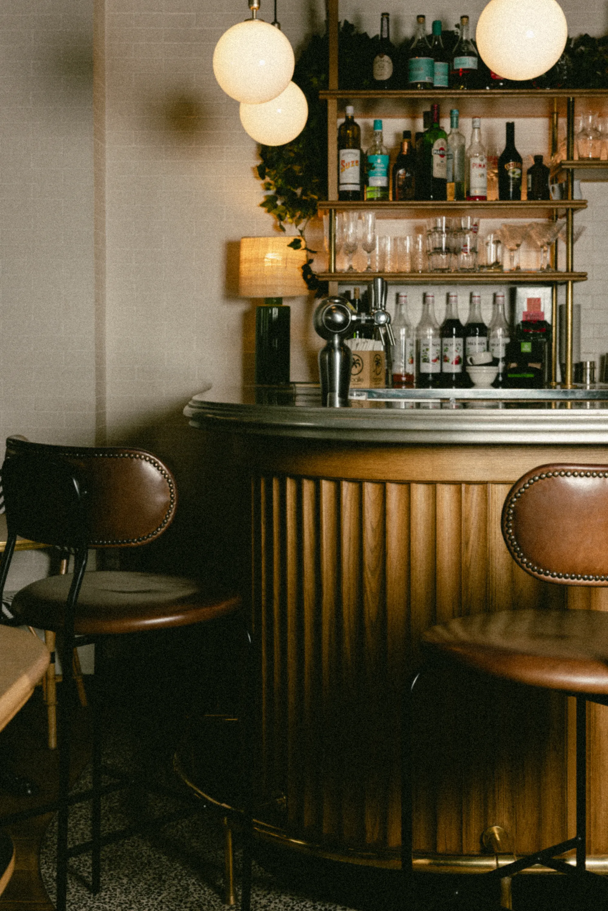 un bar en bois cannelé avec tabourets en cuir, étagère à bouteilles éclairée de suspensions globes