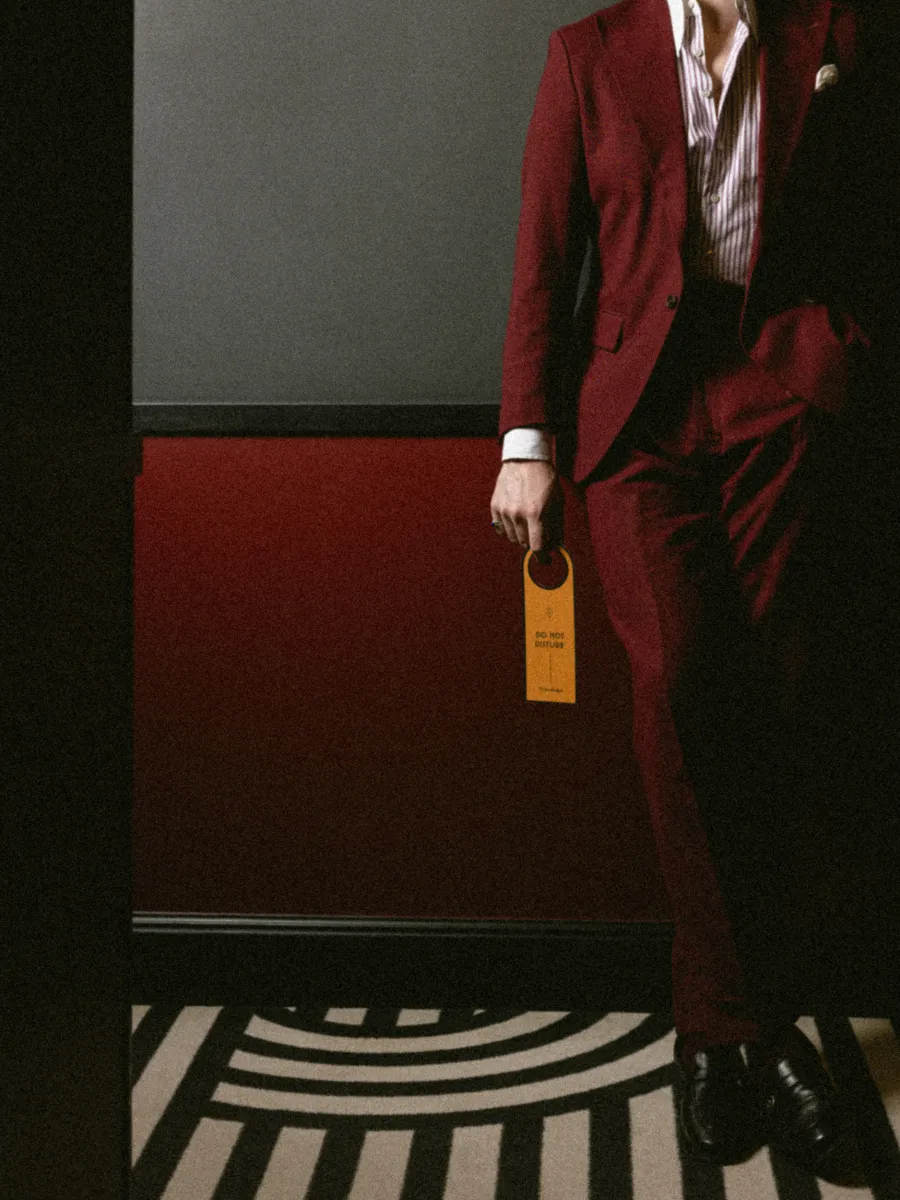 un homme en costume bordeaux tenant une carte-clé orange, debout sur le tapis à motifs arqués noir et blanc