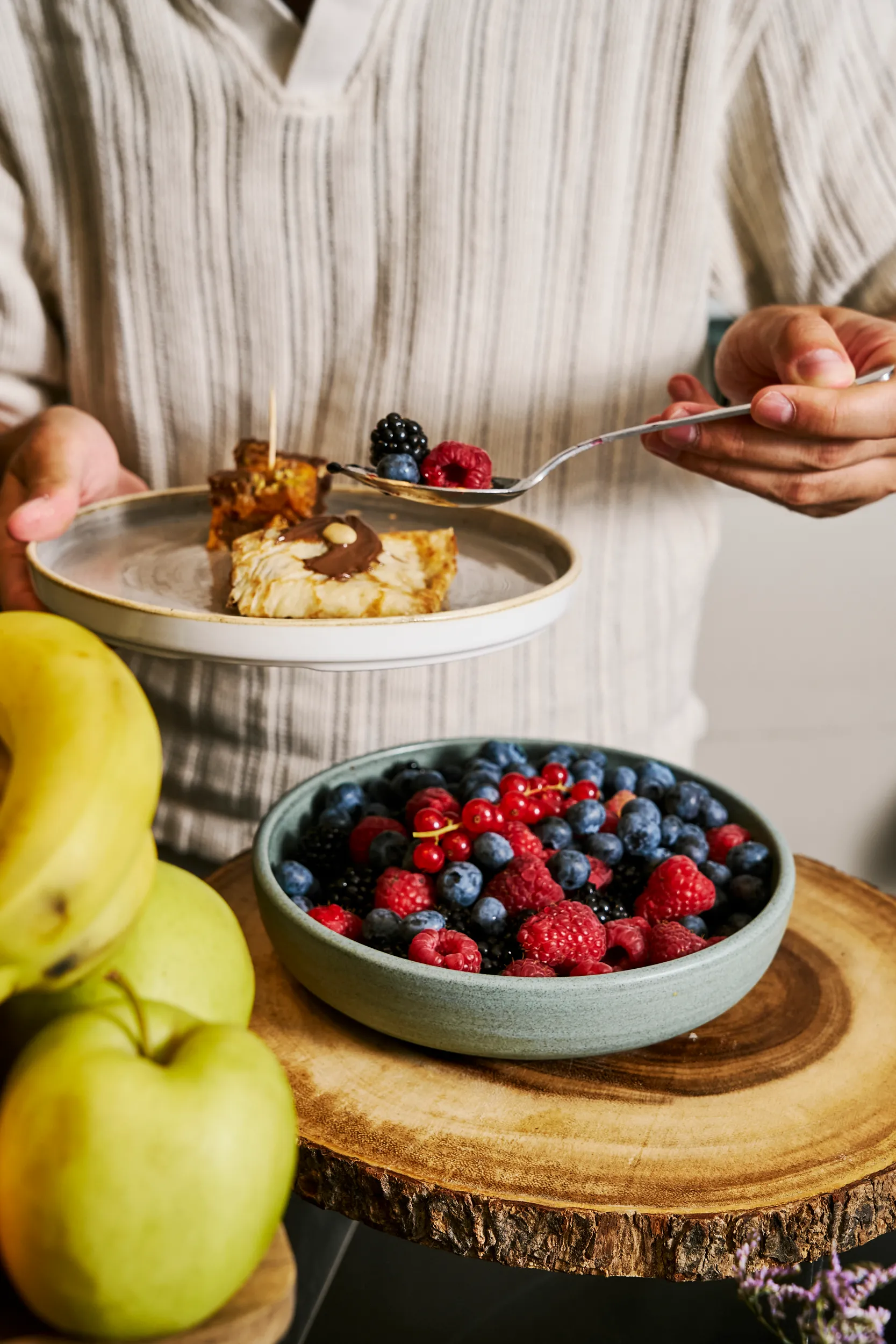 Homme se servant de fruits rouges à la cuillère au-dessus d'un bol de baies, assiette de pâtisserie et fruits frais à côté