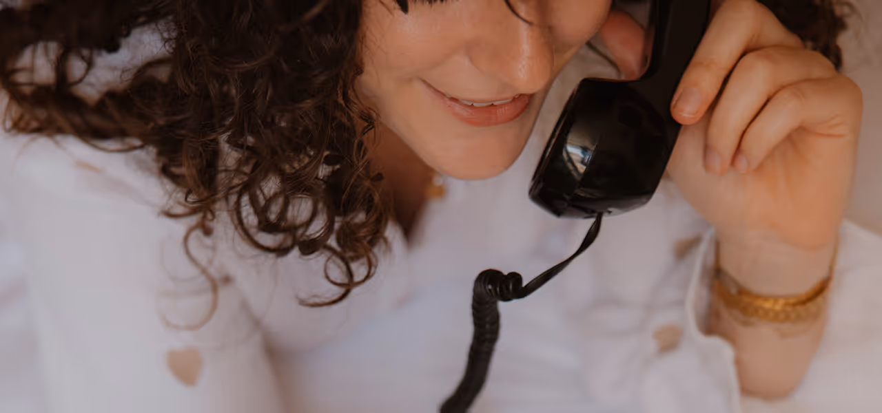 Femme souriante tenant un combiné téléphonique noir près de son oreille.
