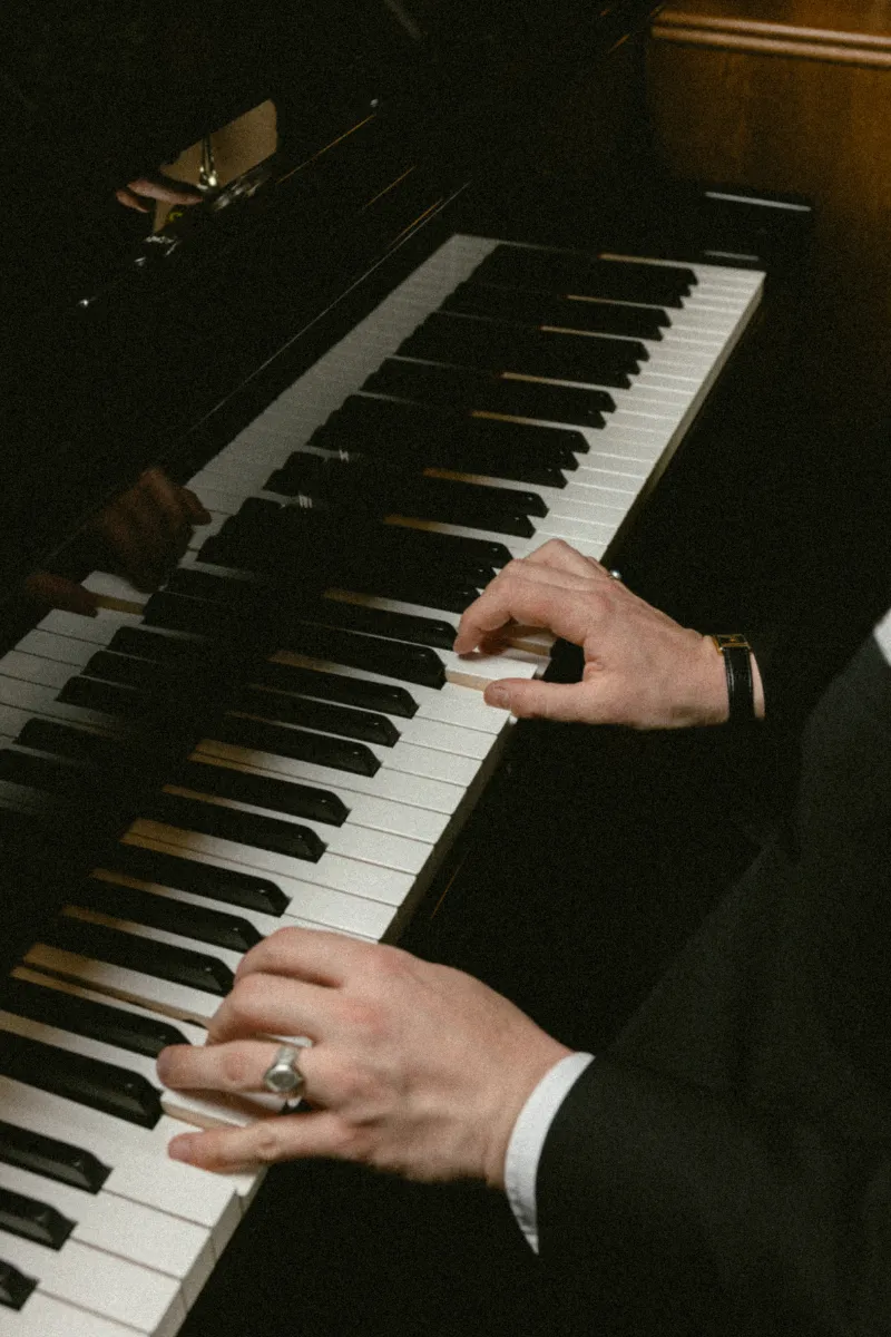Mains d'un pianiste jouant sur un piano à queue noir avec des touches blanches et noires visibles.