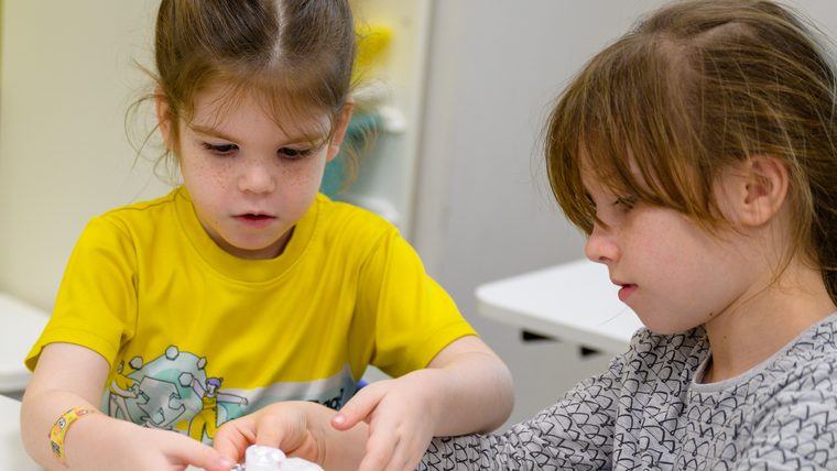 Two girls working together with a small dropper bottle, hands close, both concentrating.