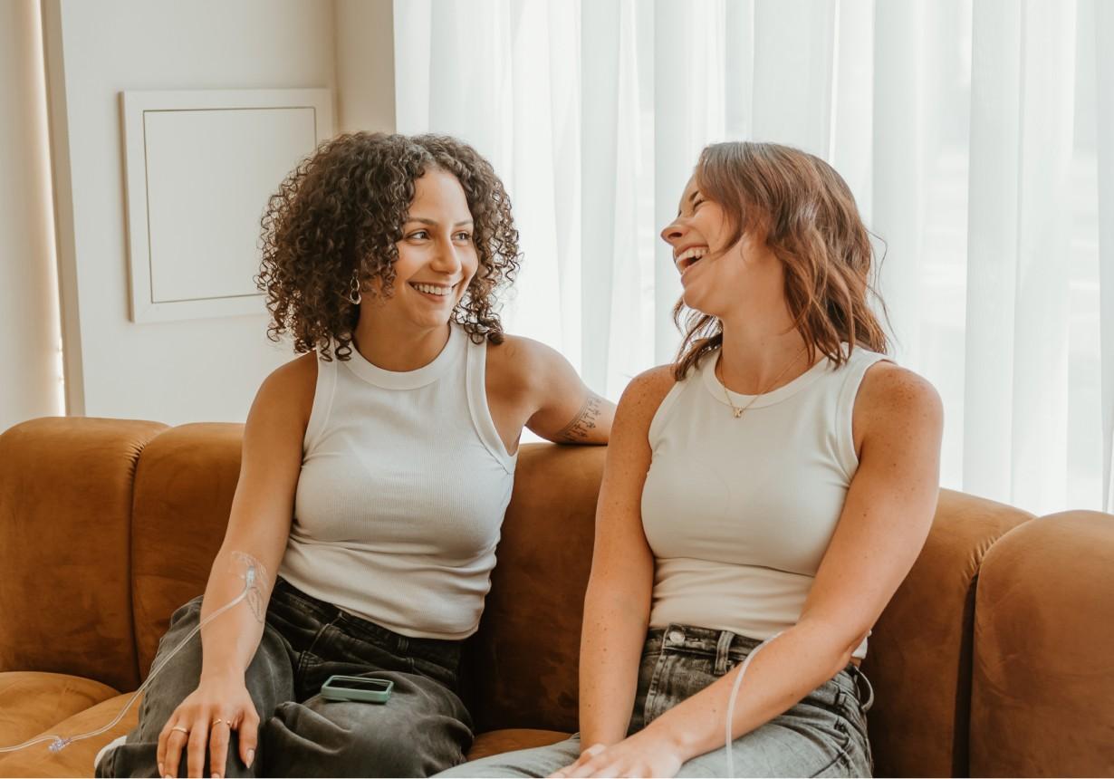 A couple of women sitting on top of a brown couch.