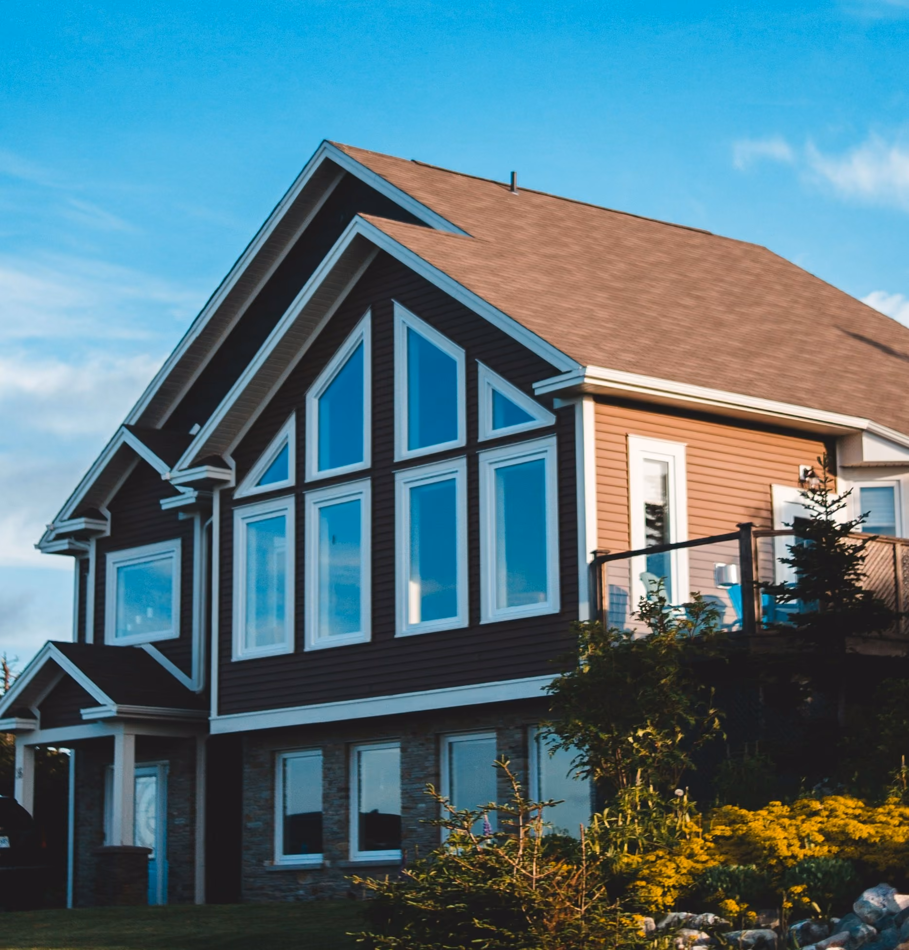 Large modern house with multiple large windows and landscaped yard with shrubs and flowers.