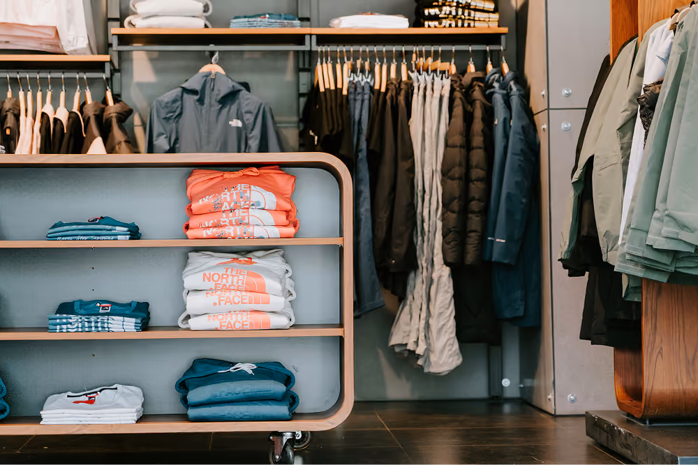 Folded and hanging outdoor jackets and shirts displayed in a retail clothing store.