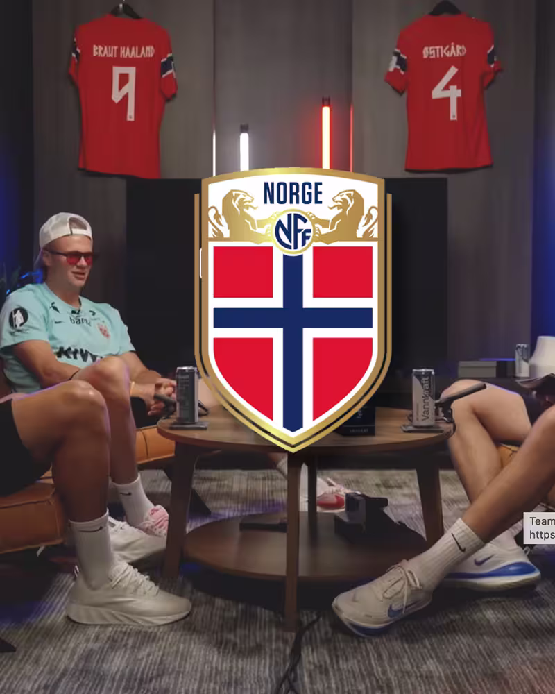 Two men seated facing each other with Norwegian Football Federation logo and jerseys in background.