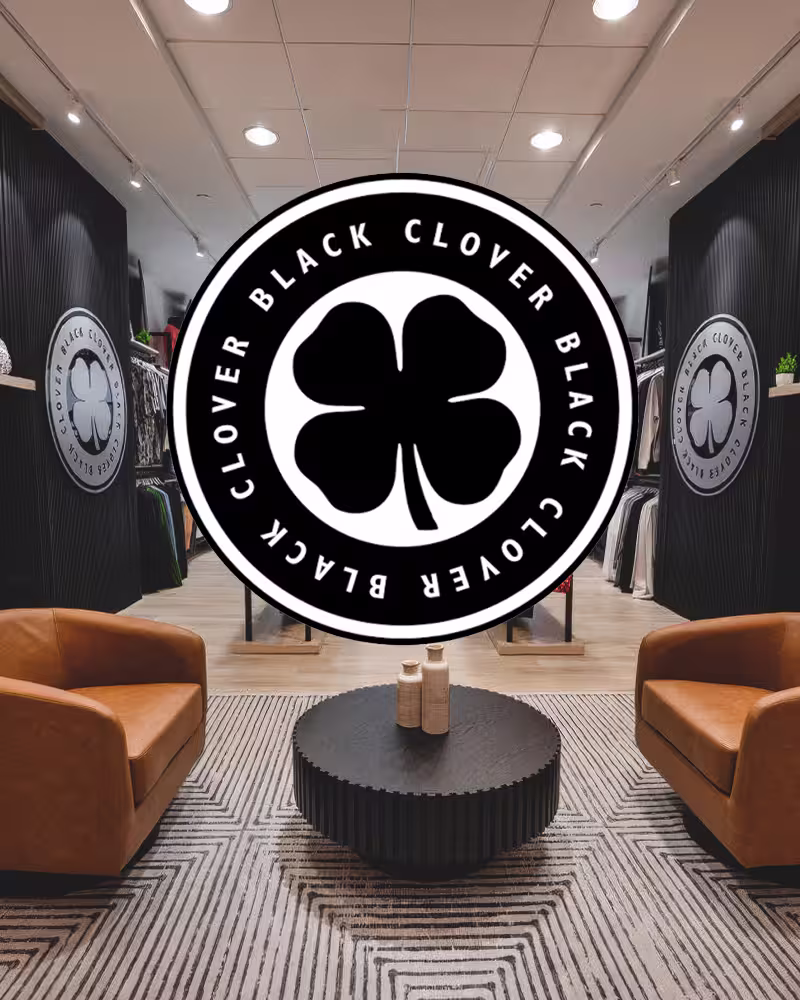 Modern retail space with two leather chairs, black round table, striped rug, and Black Clover logo overlay.