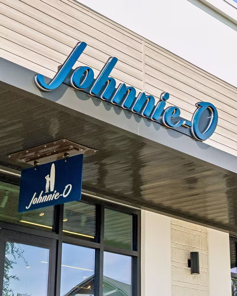 Storefront sign reading Johnnie-O in blue letters above entrance with a hanging blue sign below.