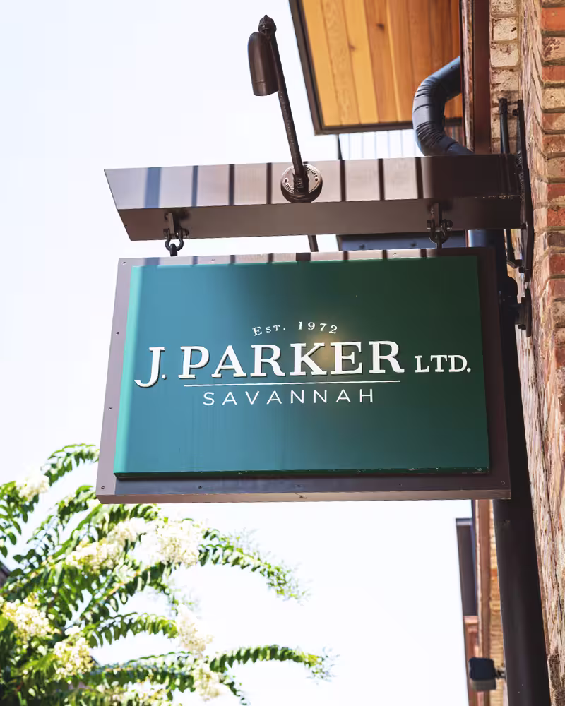 Green sign reading 'J. Parker Ltd. Savannah Est. 1972' hanging outside a brick building.