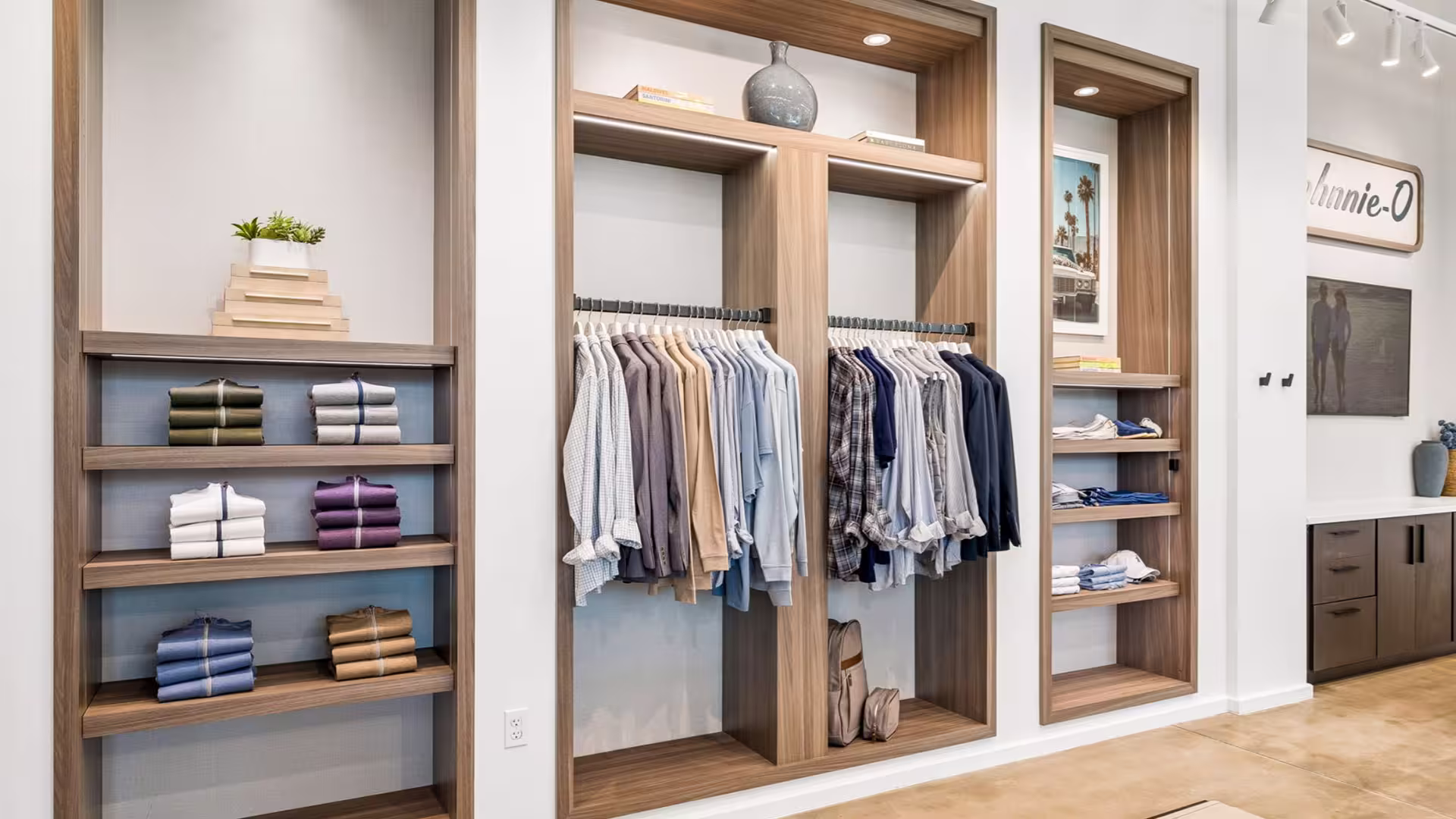 Modern retail store interior with wooden shelves displaying folded clothes and hanging shirts.