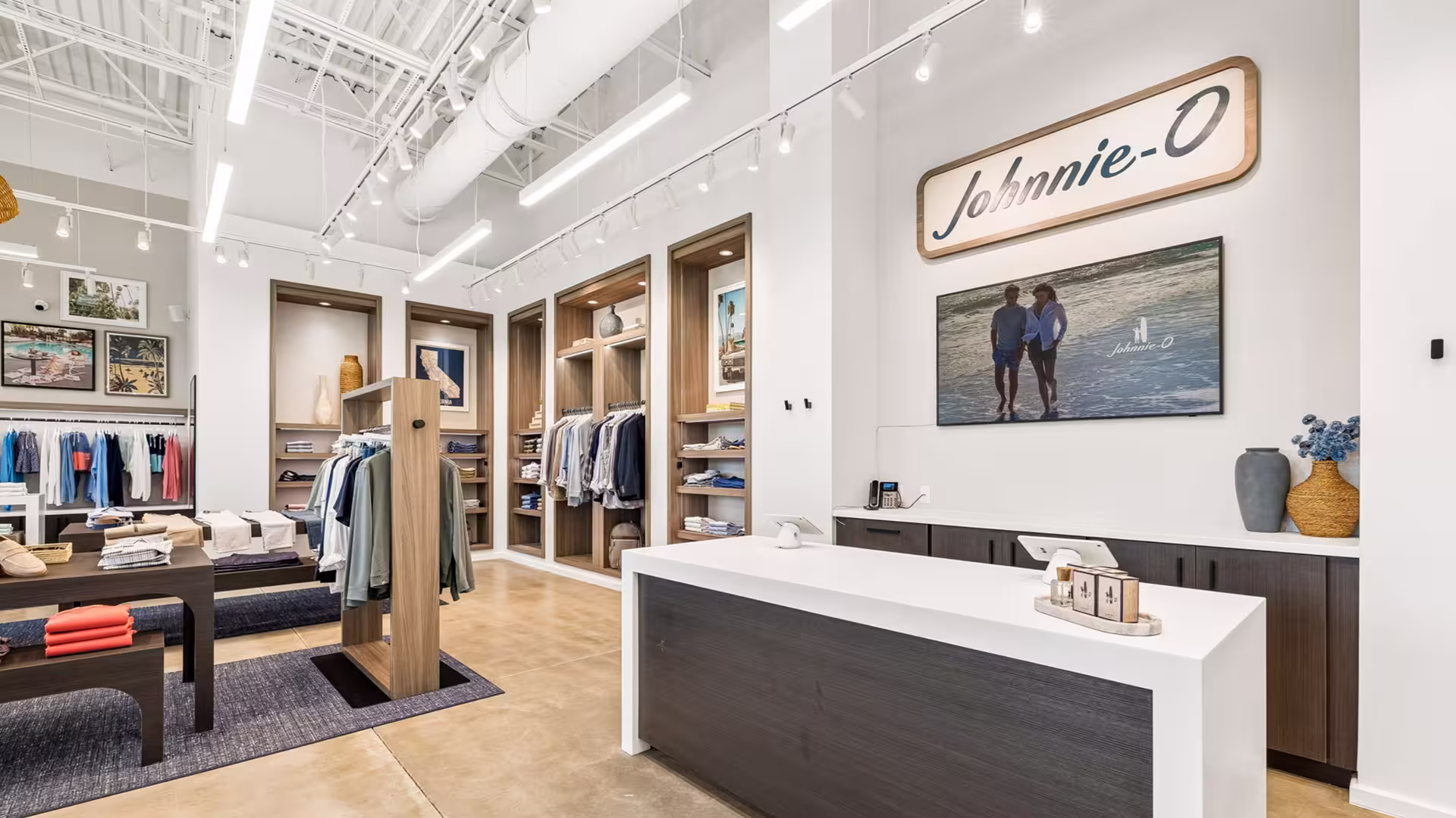 Bright modern clothing store interior with racks, shelves, and white checkout counter under Johnnie-O sign.