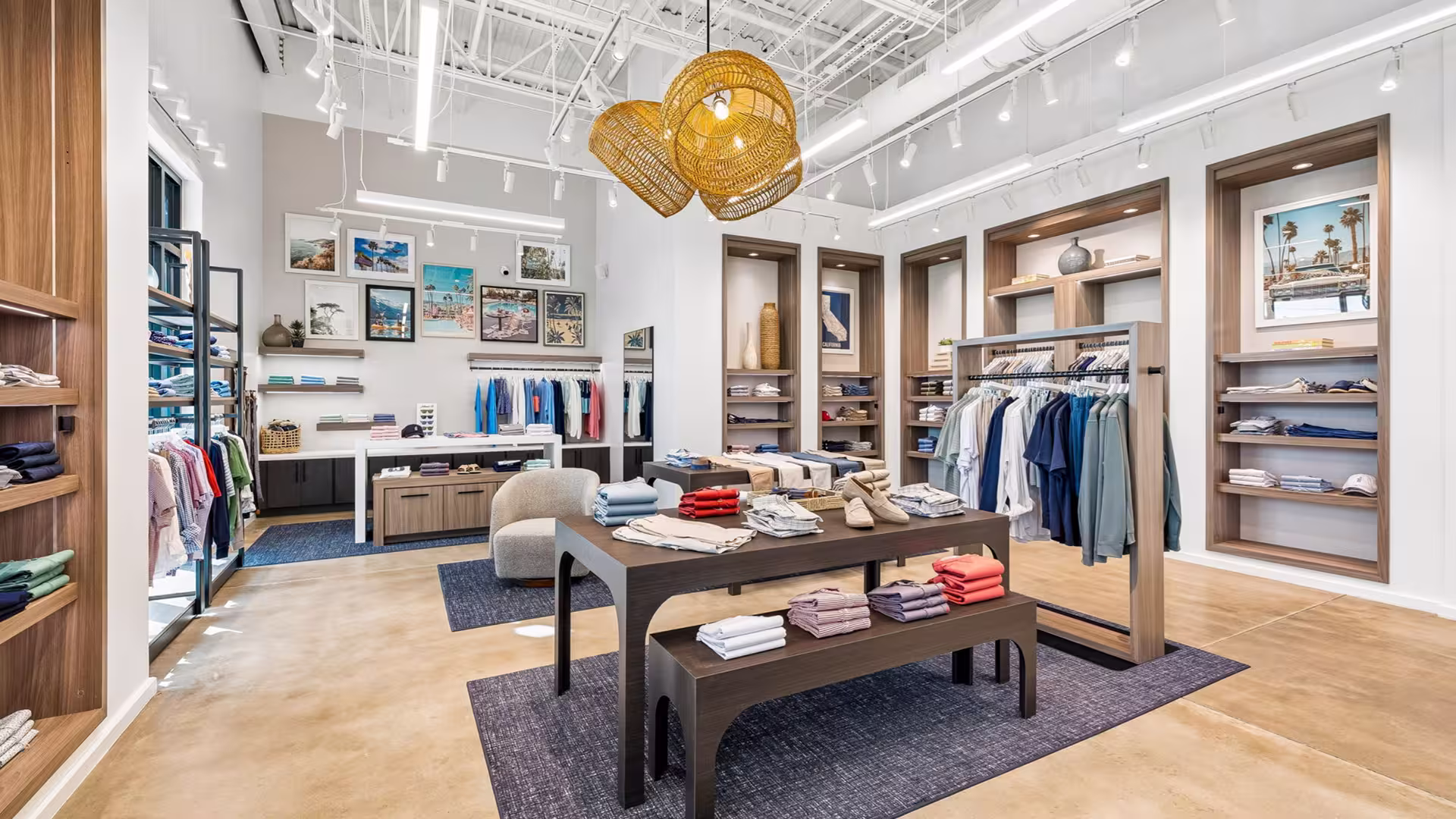 Modern clothing store interior with folded clothes on tables, racks of shirts, and framed photos on walls.