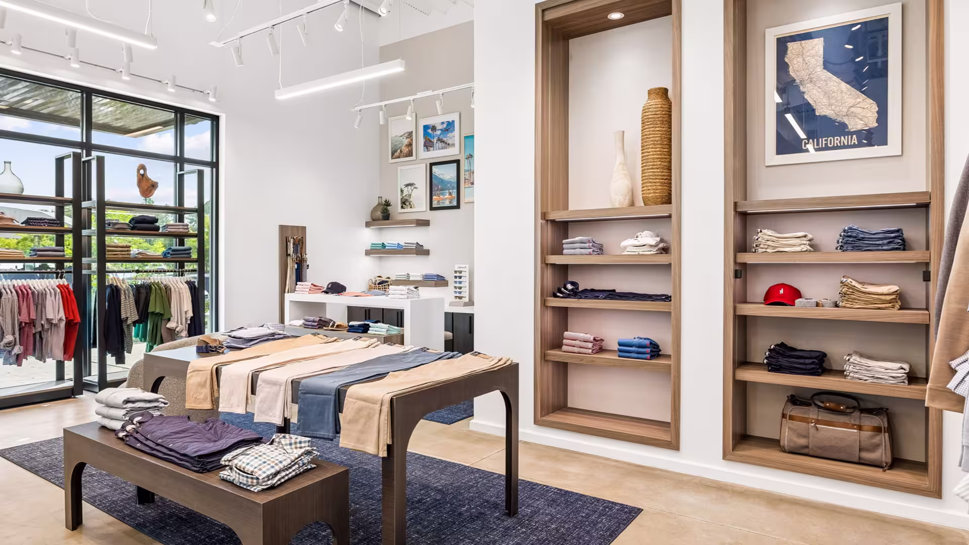 Bright retail store interior with casual folded clothes, hanging shirts, framed photos, and decorative items.