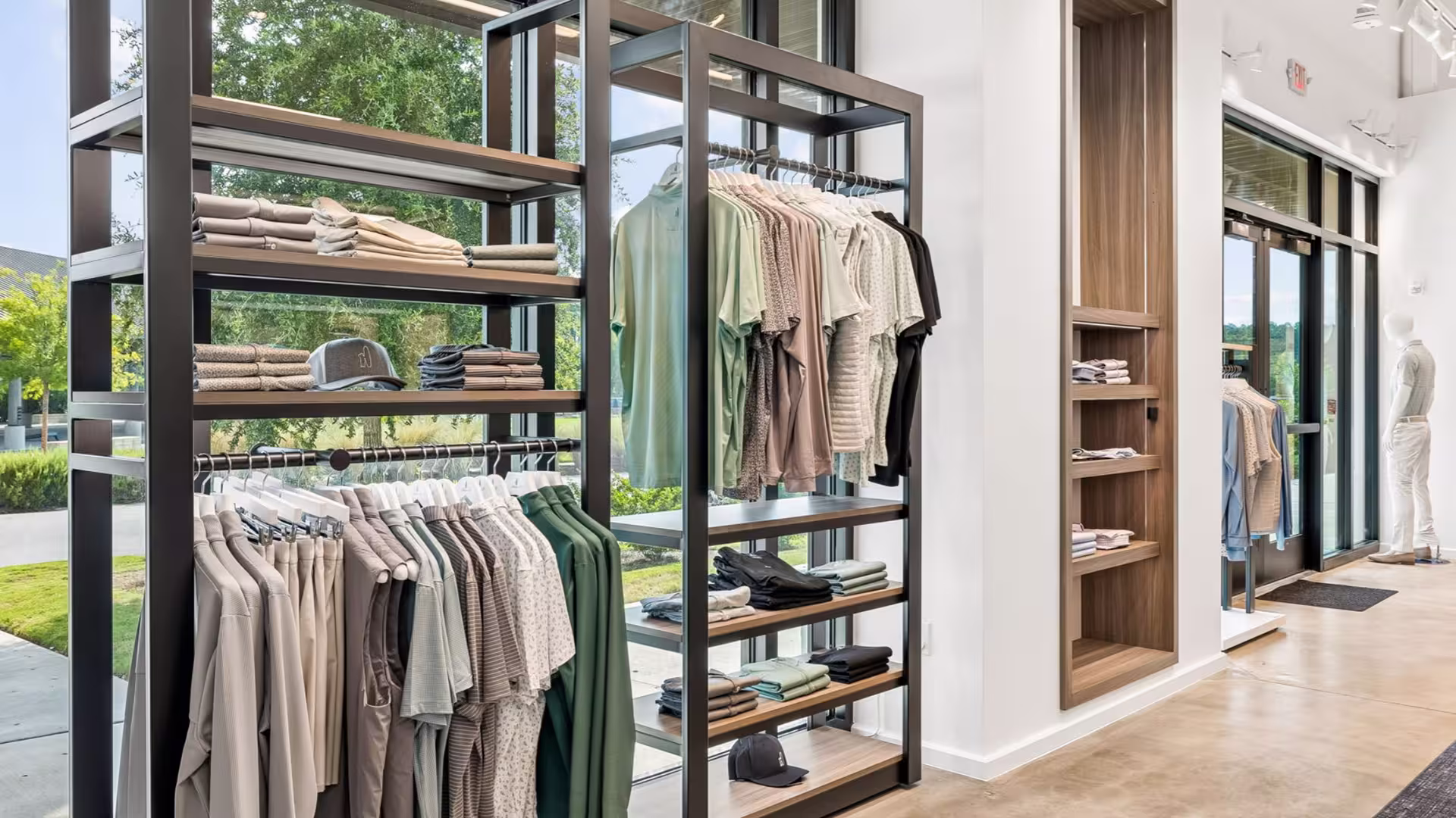 Modern clothing rack with folded clothes, hats, and hanging shirts in a bright store with large windows.