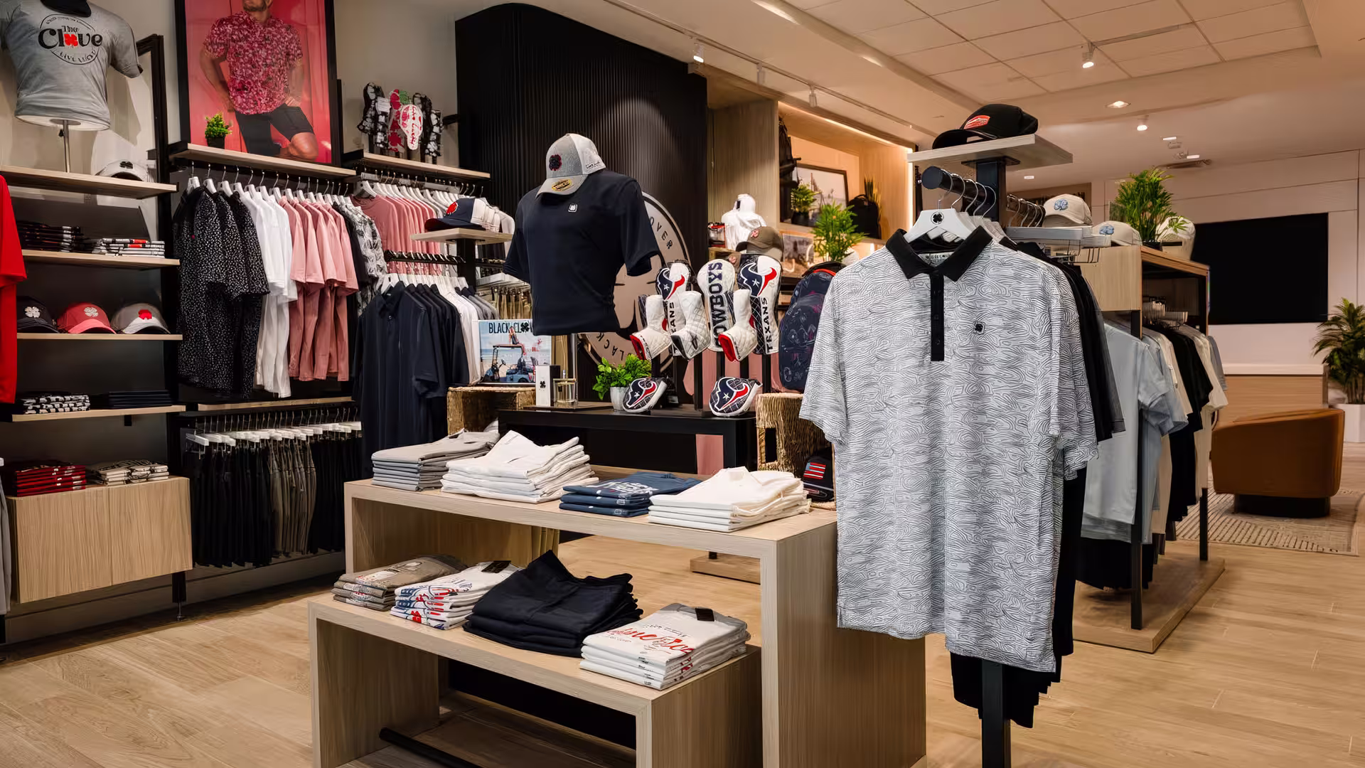 Clothing store interior with polo shirts, caps, folded tees, and golf club headcovers on display.